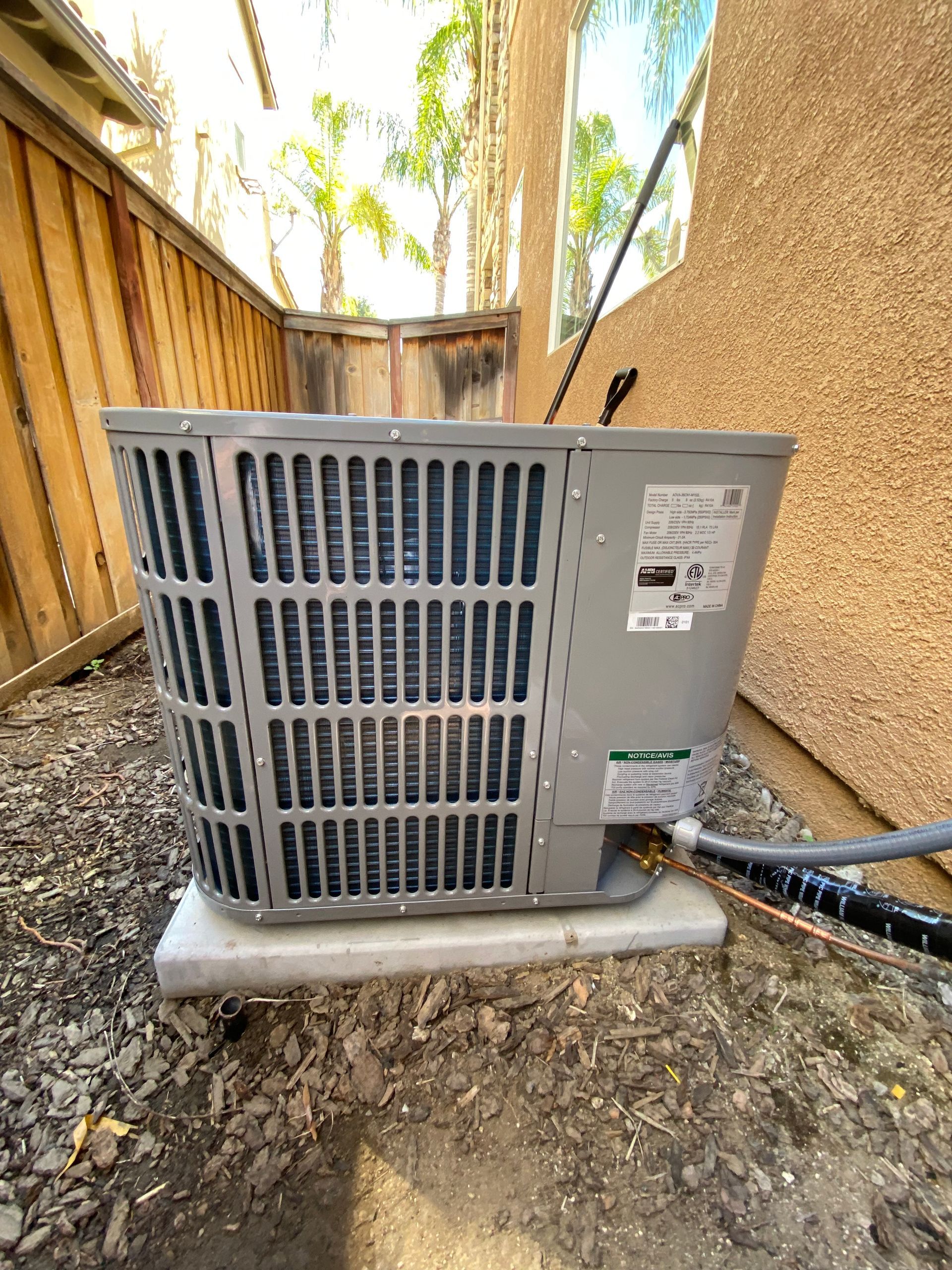 A gray air conditioner is sitting on top of a white shelf outside of a house.