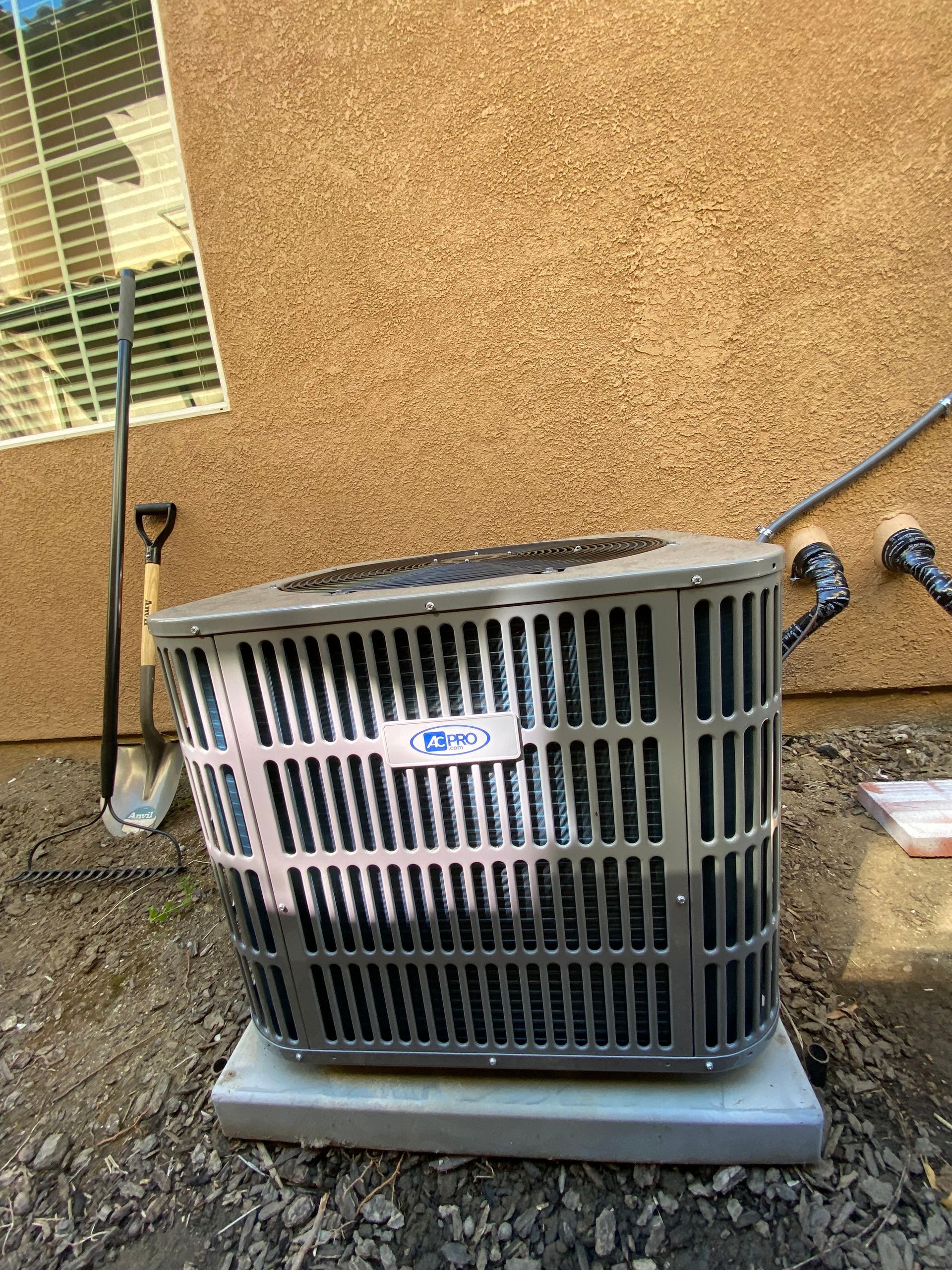An air conditioner is sitting outside of a house next to a window.