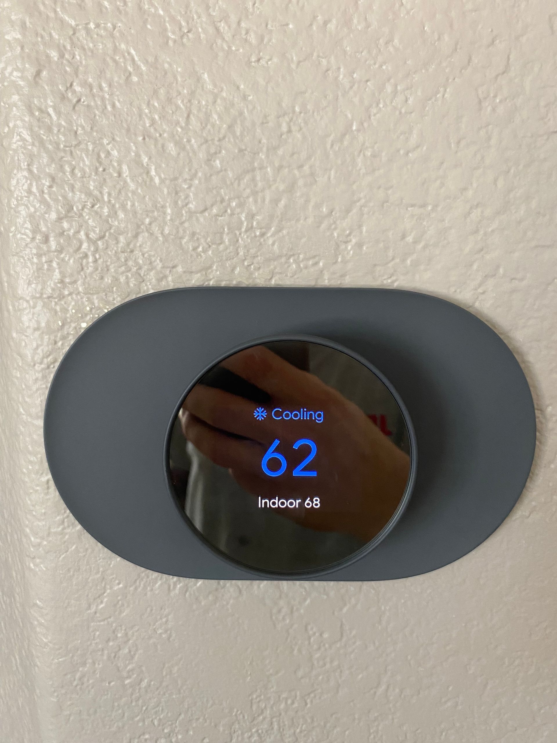 A person is taking a picture of a thermostat on a wall.