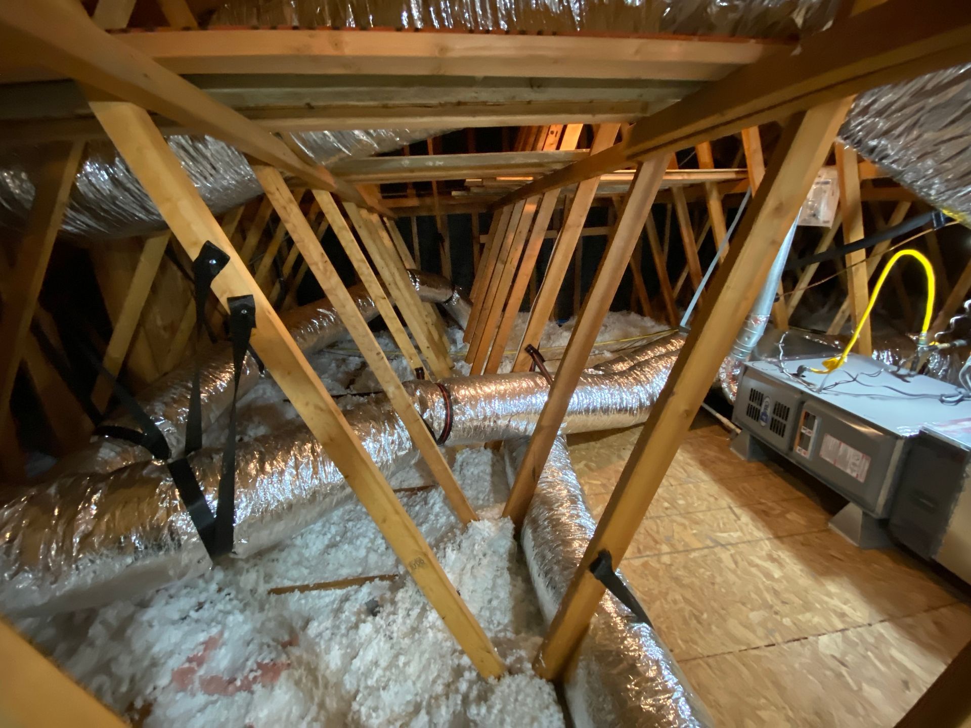 An attic with a lot of wooden beams and ducts.