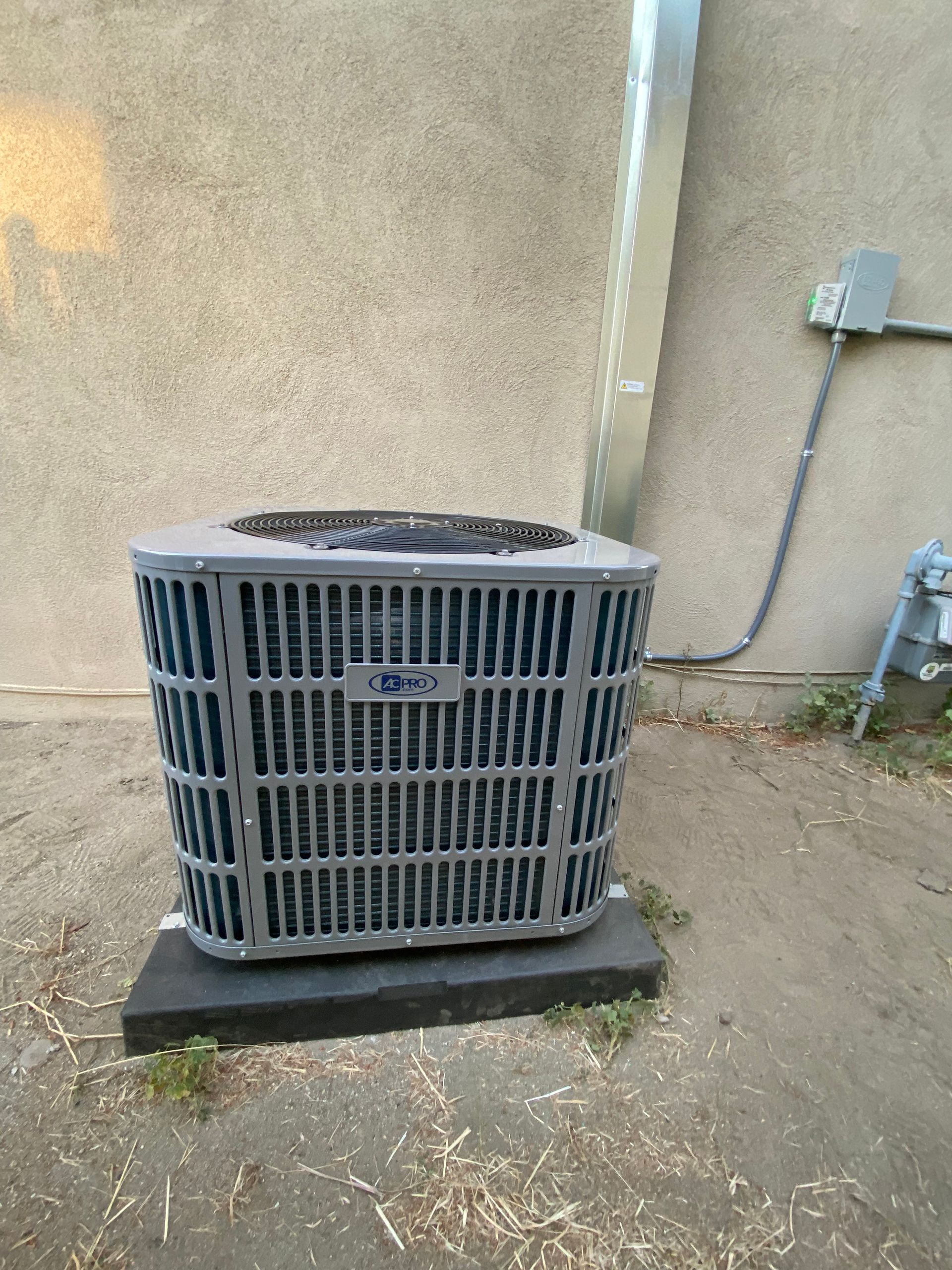 A gray air conditioner is sitting on a concrete platform in front of a wall.