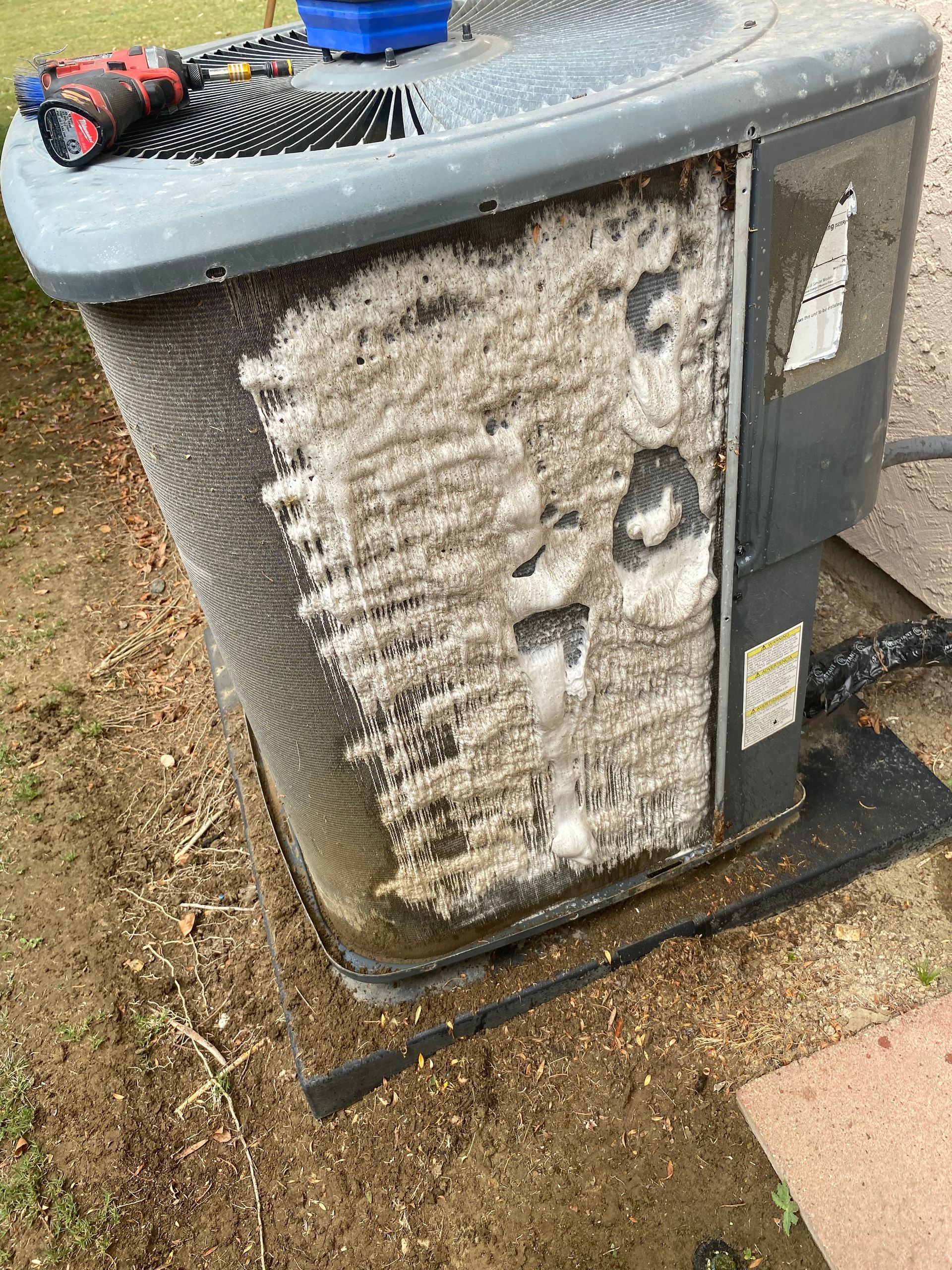 A dirty air conditioner is sitting on the ground.
