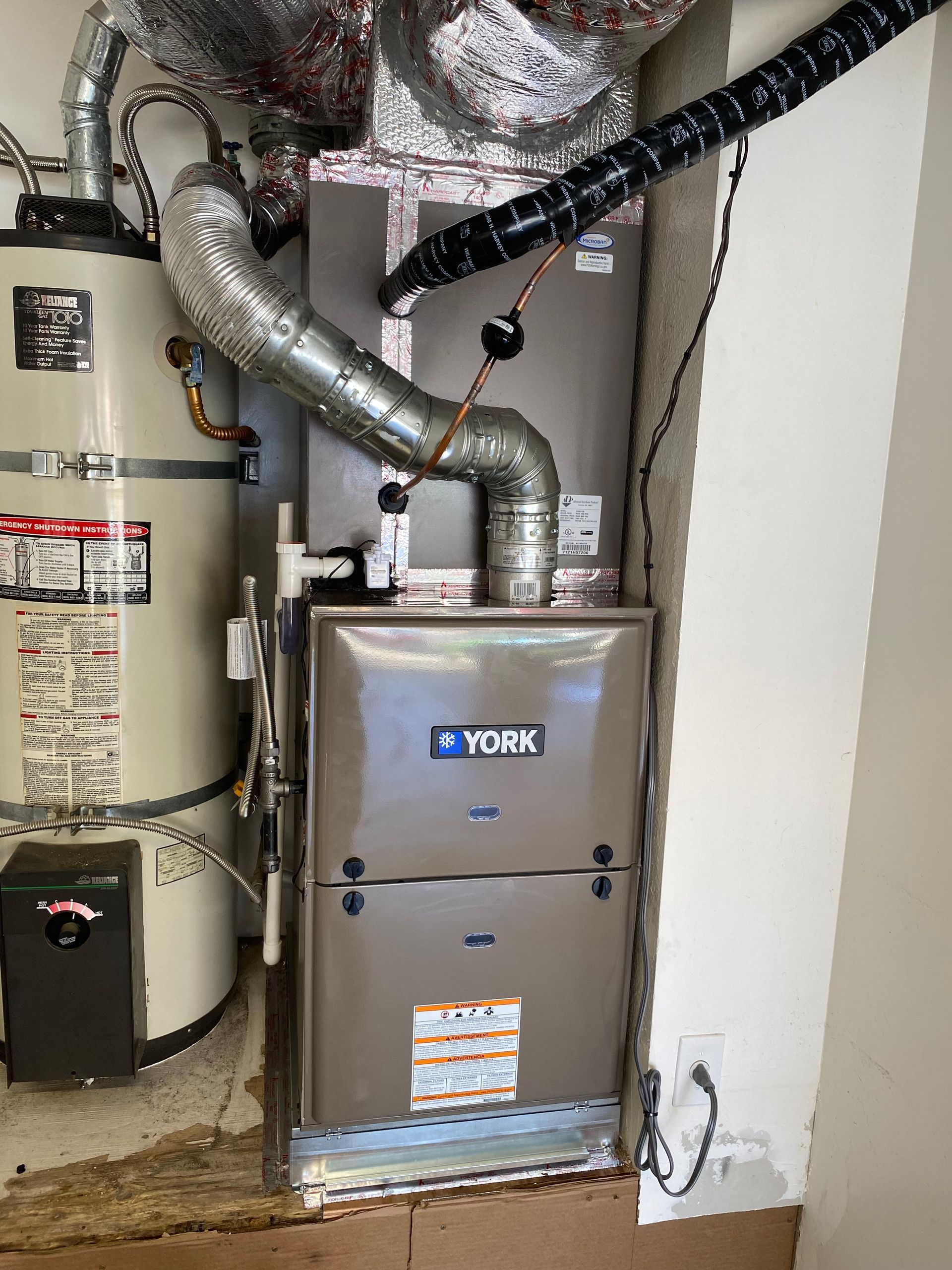 A york furnace is sitting next to a water heater in a basement.