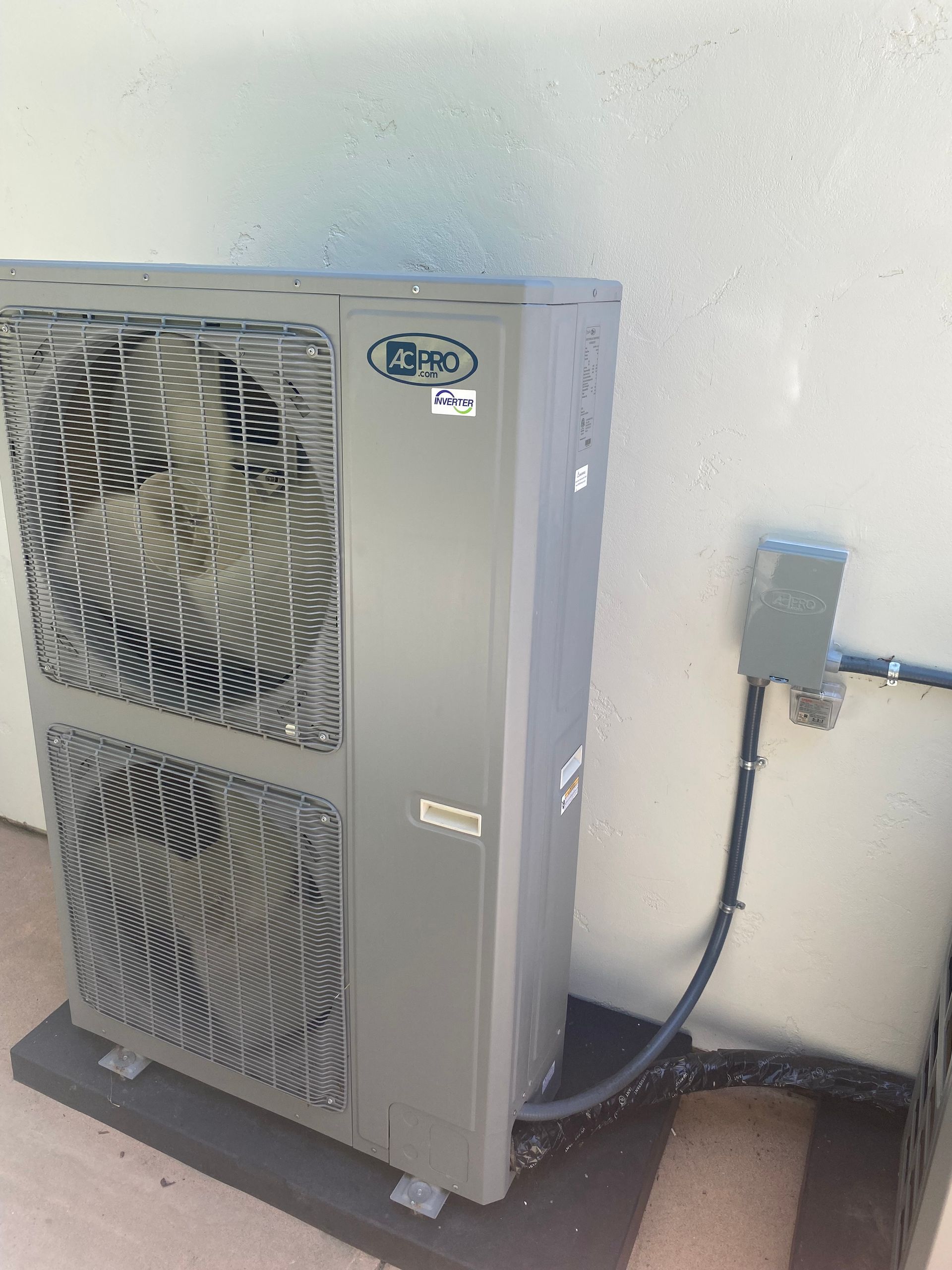 A gray air conditioner is sitting on a concrete floor next to a wall.