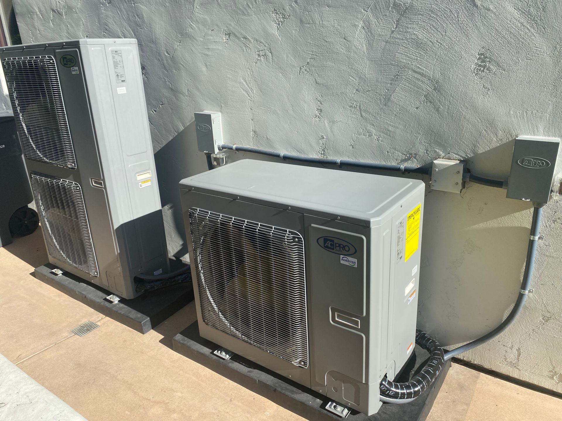 Two air conditioners are sitting next to each other on the side of a building.