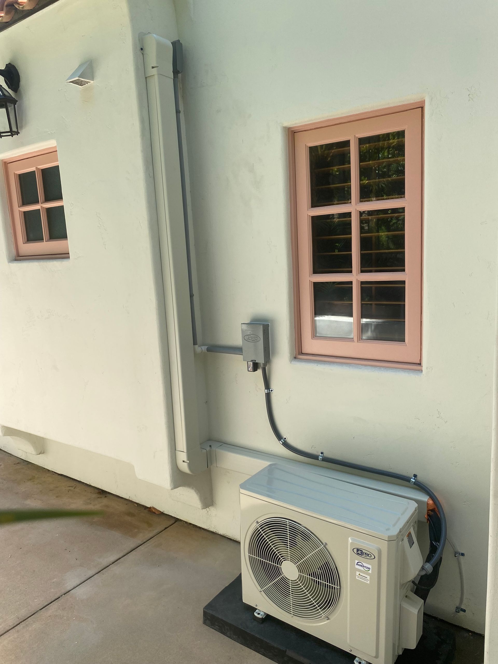An air conditioner is sitting outside of a building next to a window.