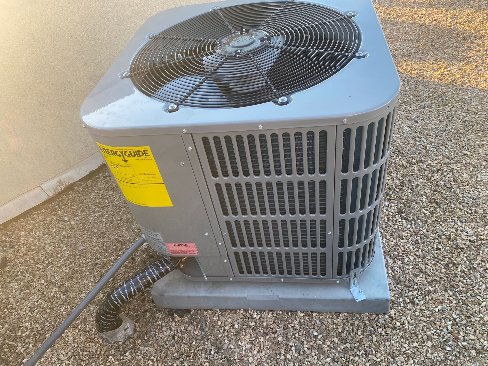 A gray air conditioner is sitting on the ground next to a wall.