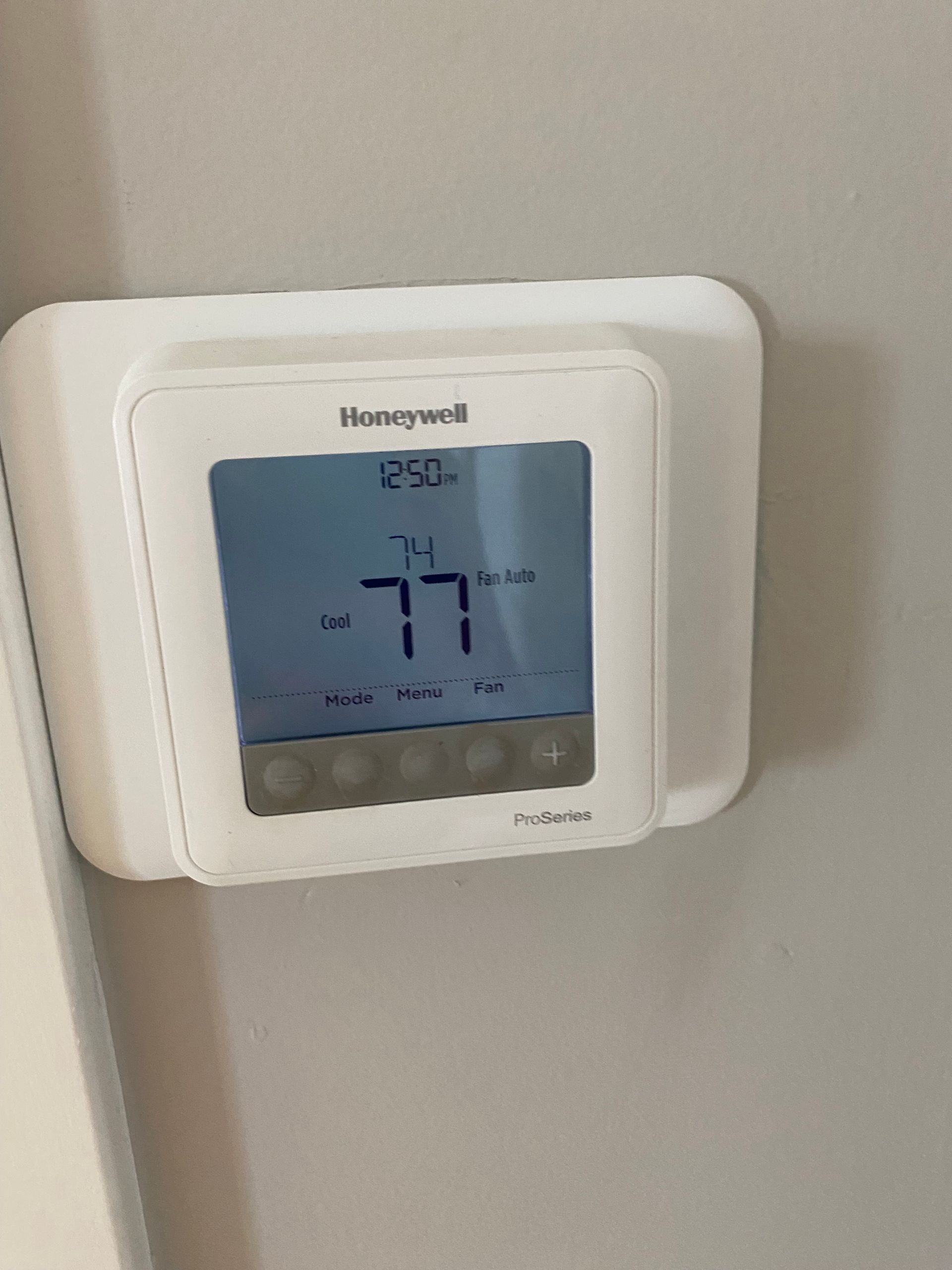 A white honeywell thermostat is hanging on a wall.