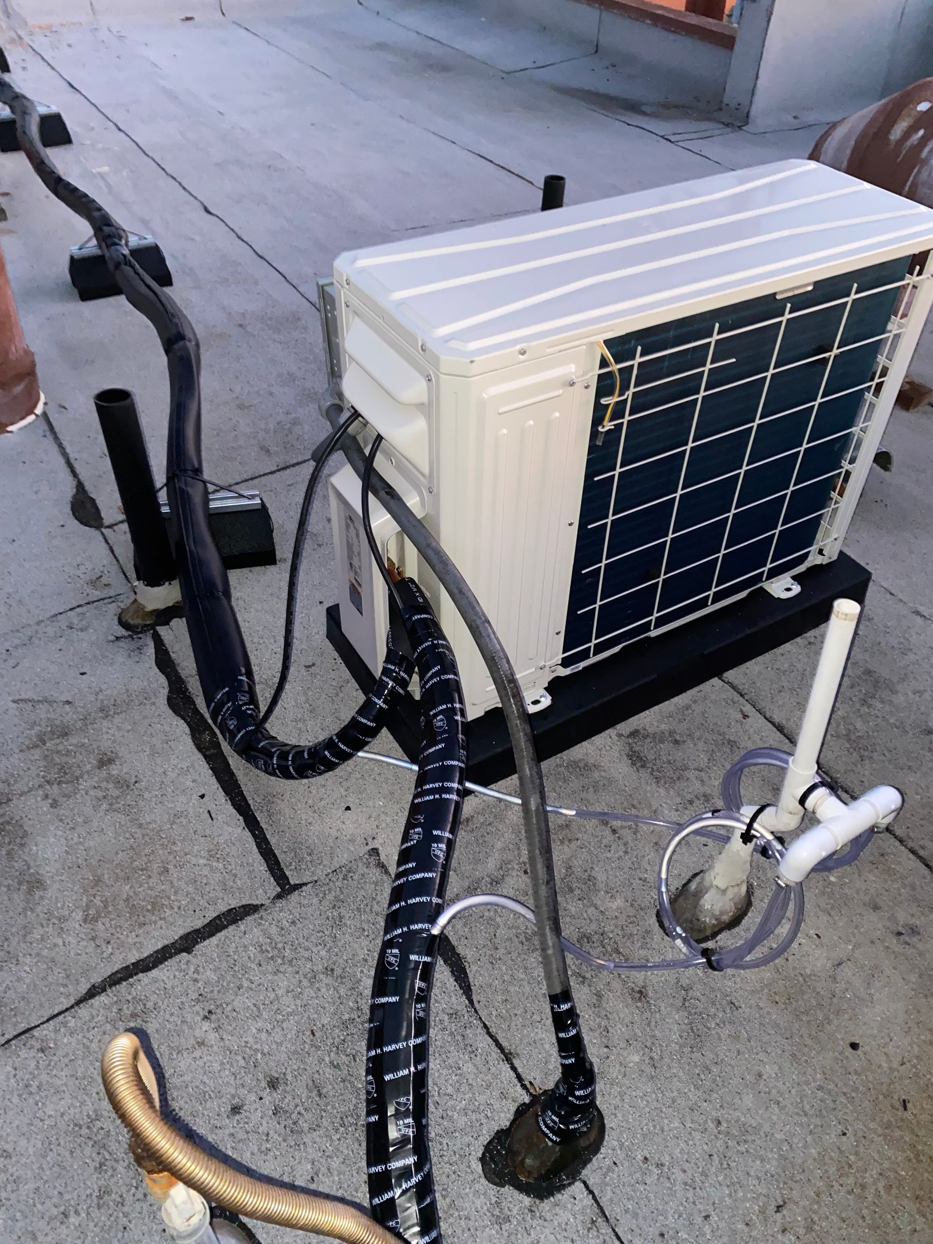 An air conditioner is sitting on the sidewalk with a hose attached to it.
