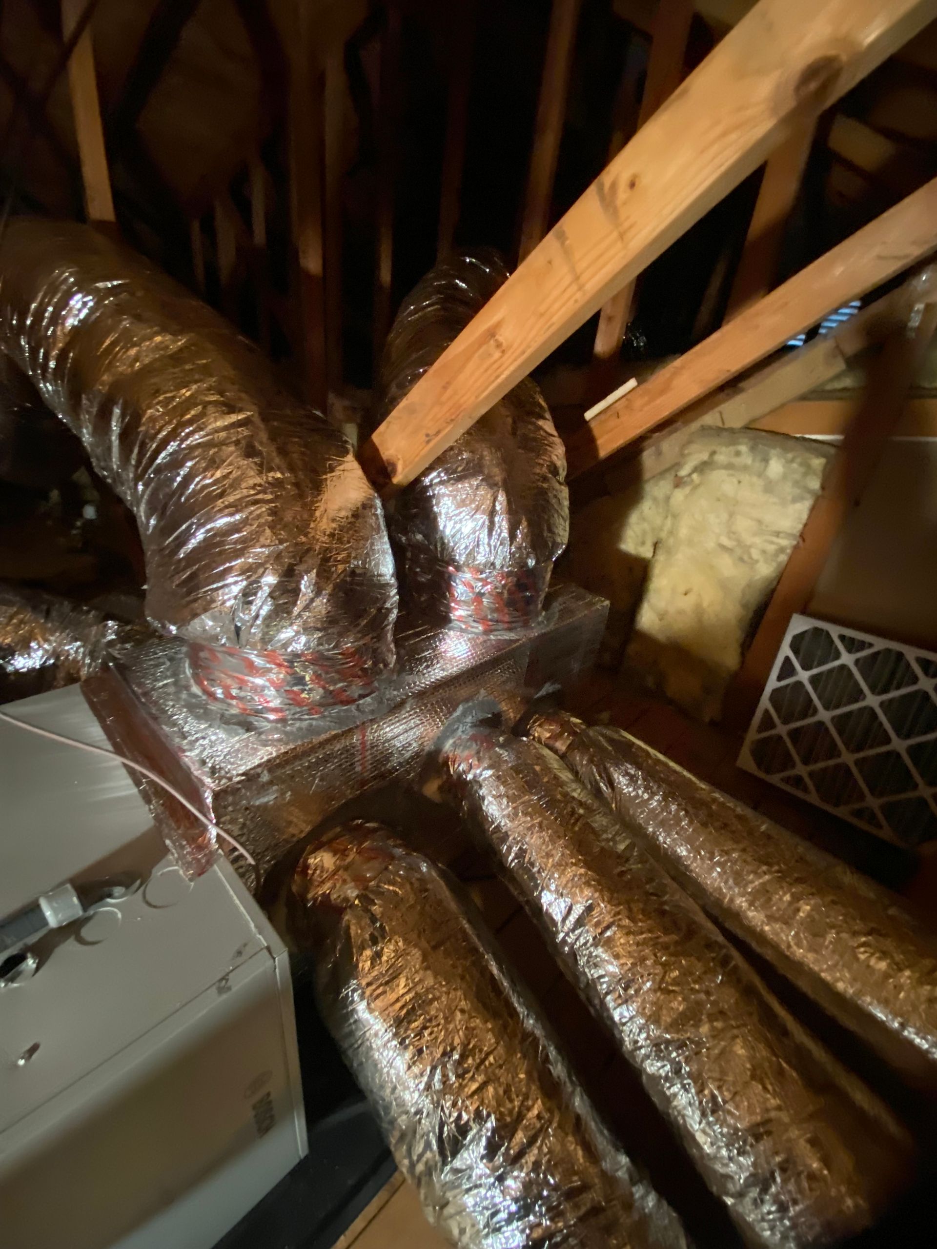 A bunch of ducts are wrapped in foil in an attic.
