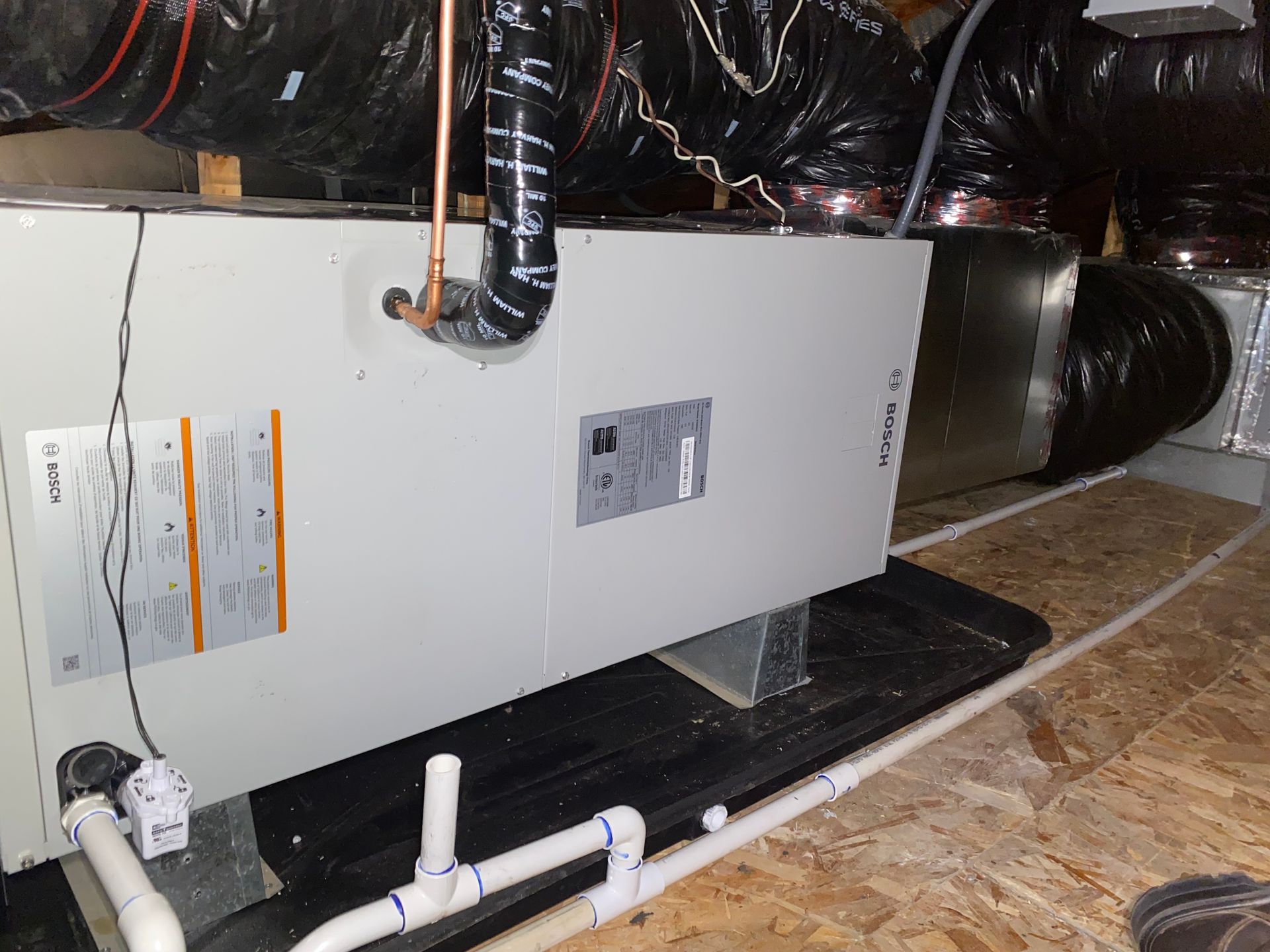 A white box is sitting on top of a wooden floor next to pipes.