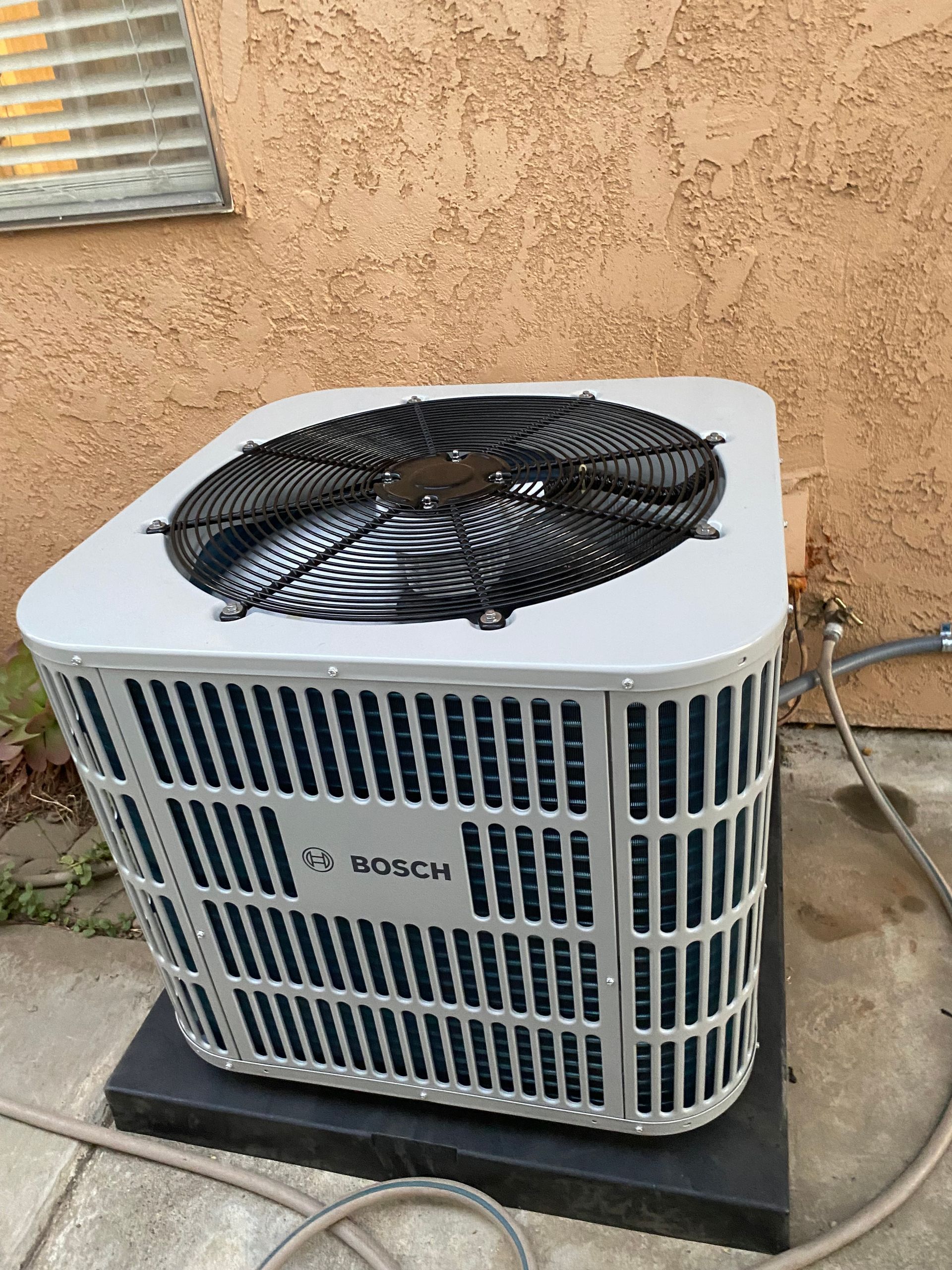 A bosch air conditioner is sitting outside of a building.