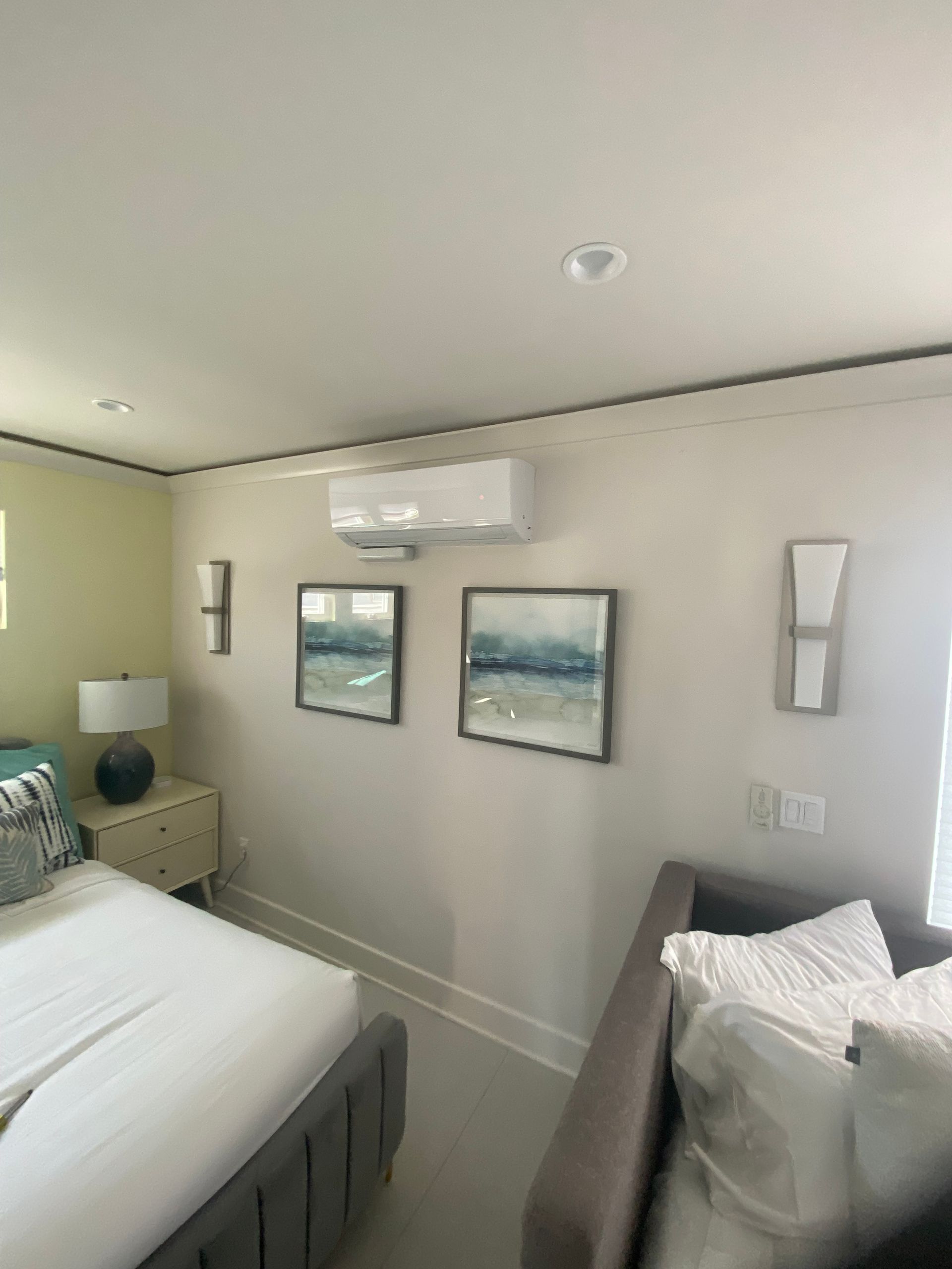 A bedroom with a bed , couch , lamps and paintings on the wall.