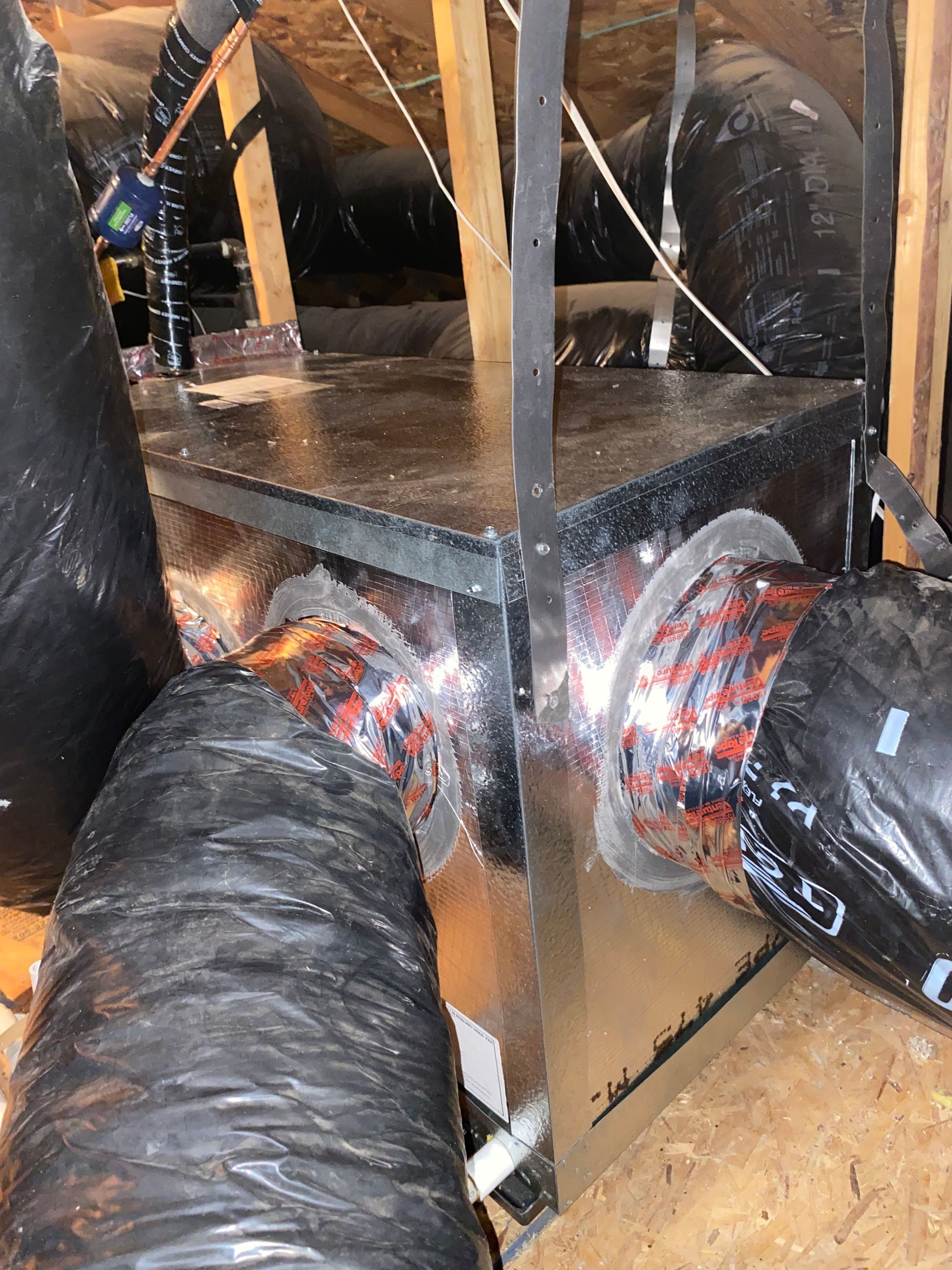 A bunch of ducts are connected to a box in the attic.
