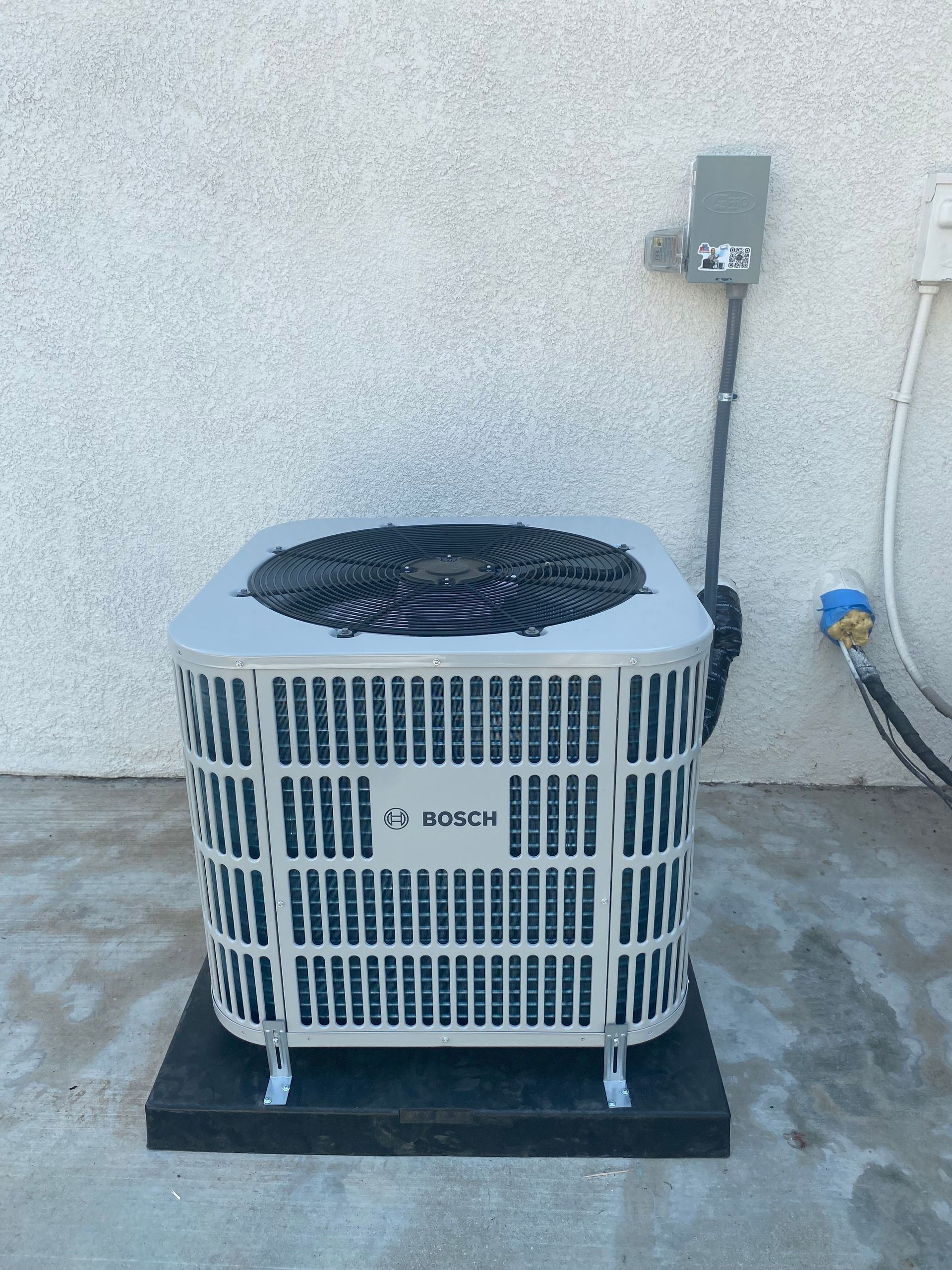 A white air conditioner is sitting on a black rubber mat in front of a white wall.