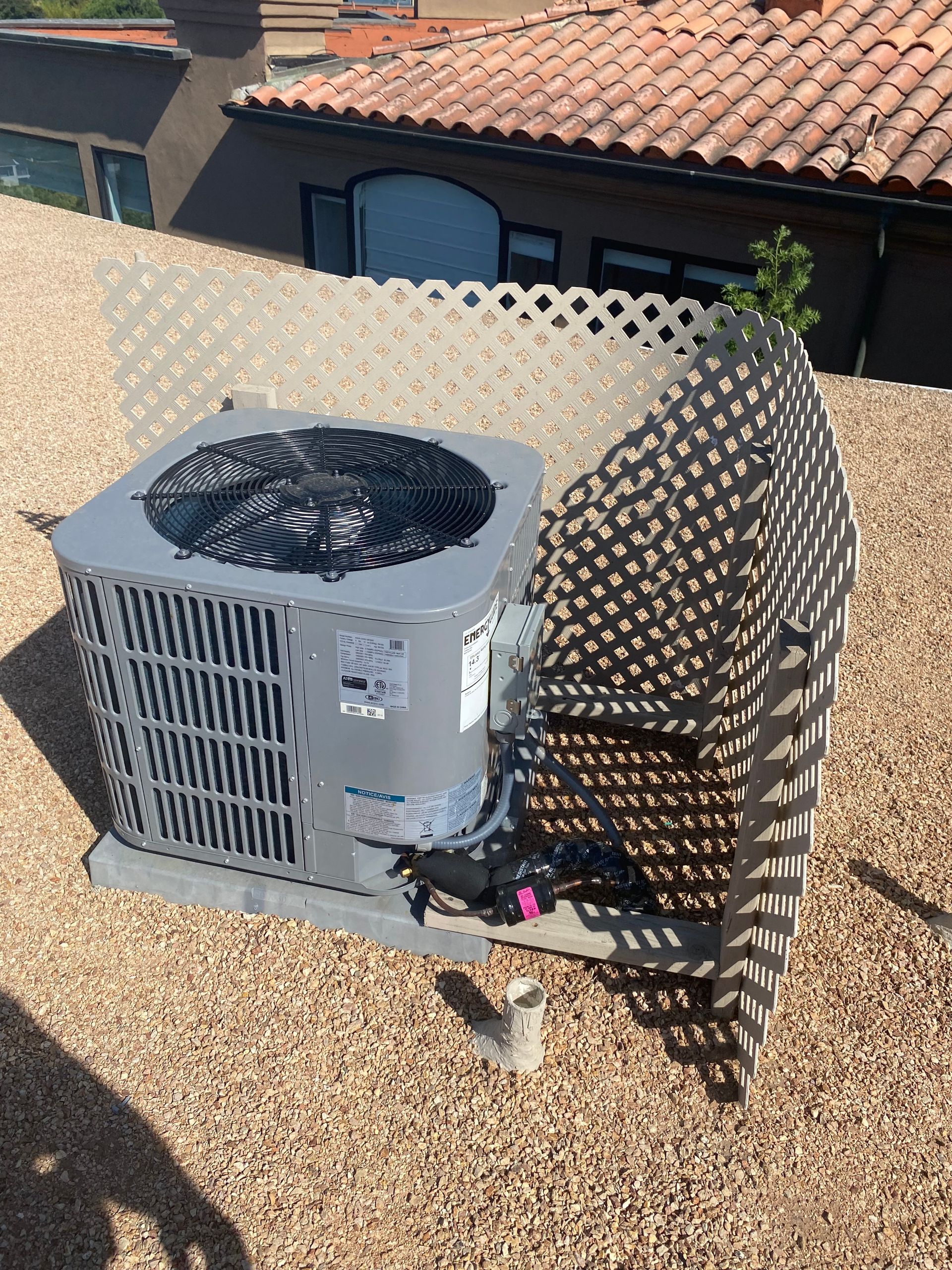 An air conditioner is sitting on top of a gravel covered roof.