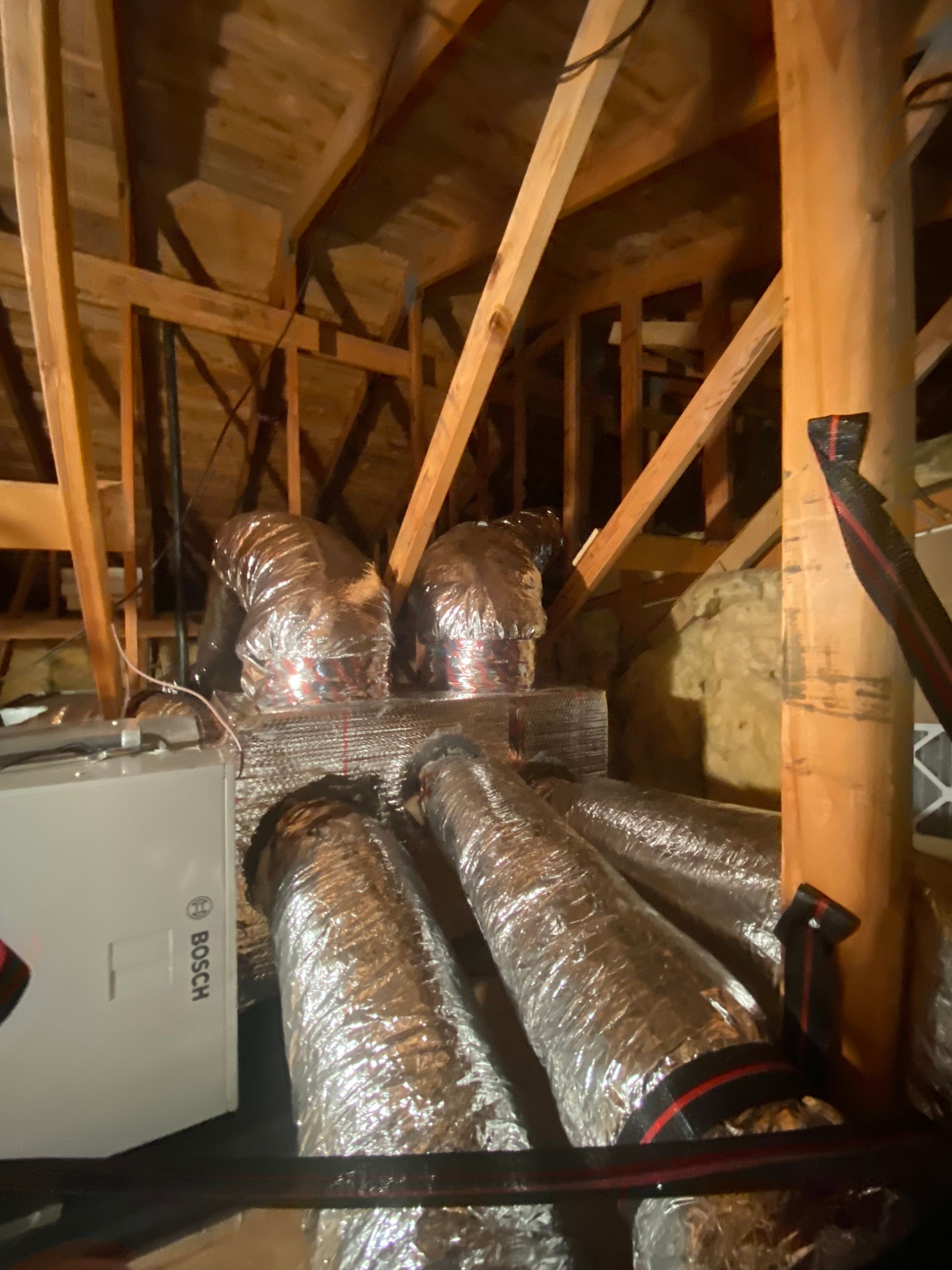 A bunch of ducts are hanging from the ceiling of an attic.