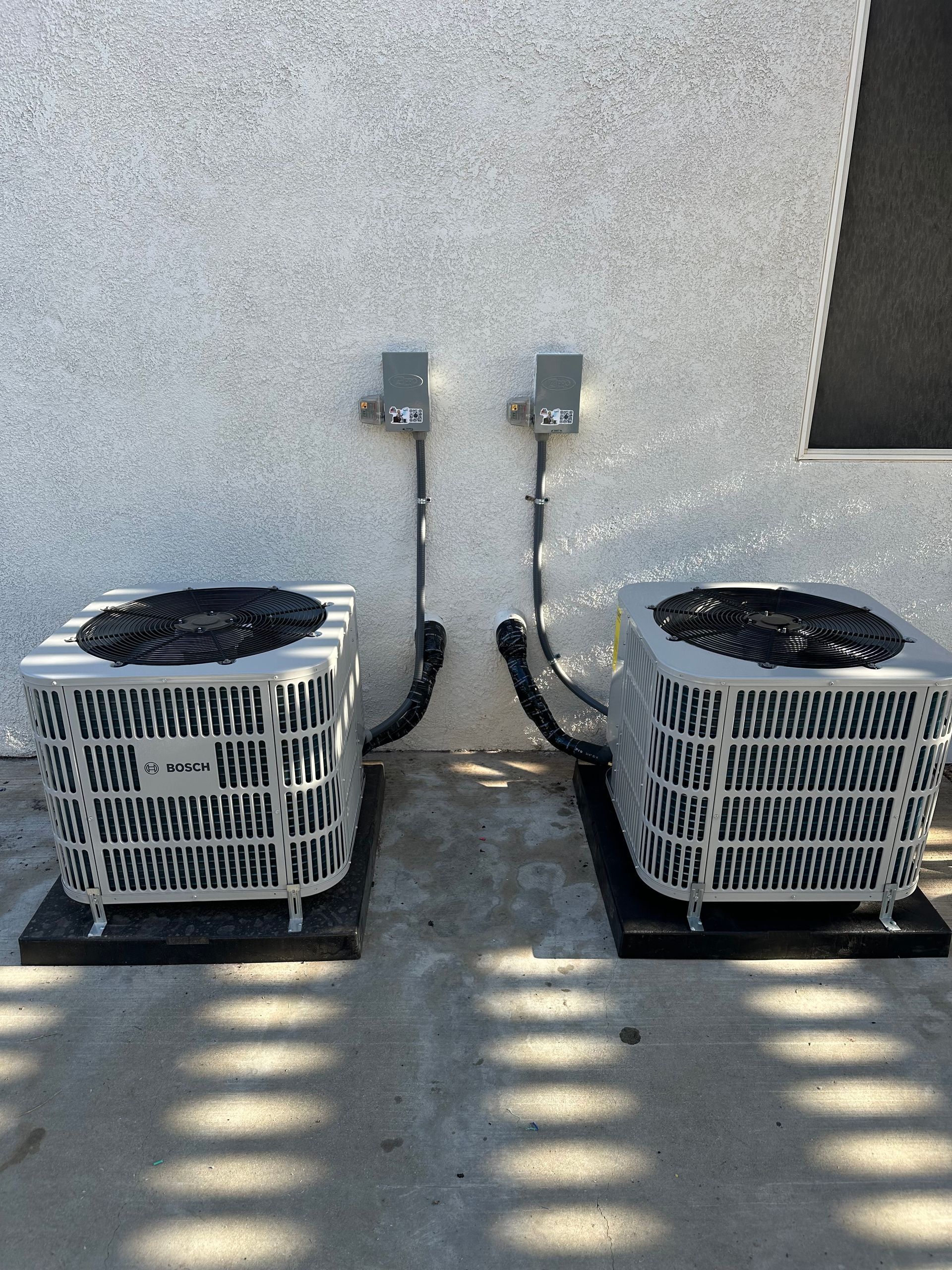 Two air conditioners are sitting next to each other on the side of a building.