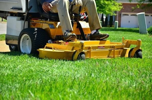 A man is riding a yellow lawn mower on a lush green lawn.