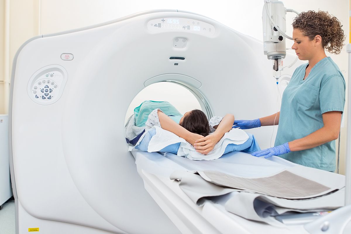 A calm, clean clinical setting showing a patient speaking with a technologist near a CT scanner.