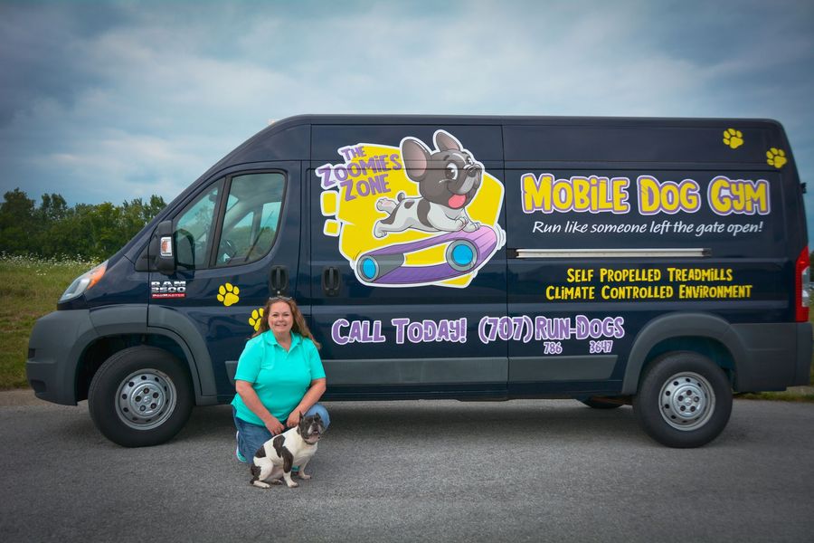 Woman kneels with a small dog in front of a dark blue van with 