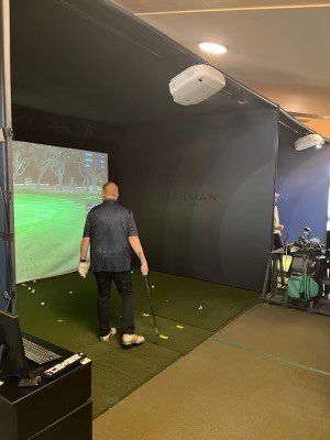 A man is standing in a golf simulator holding a golf club.