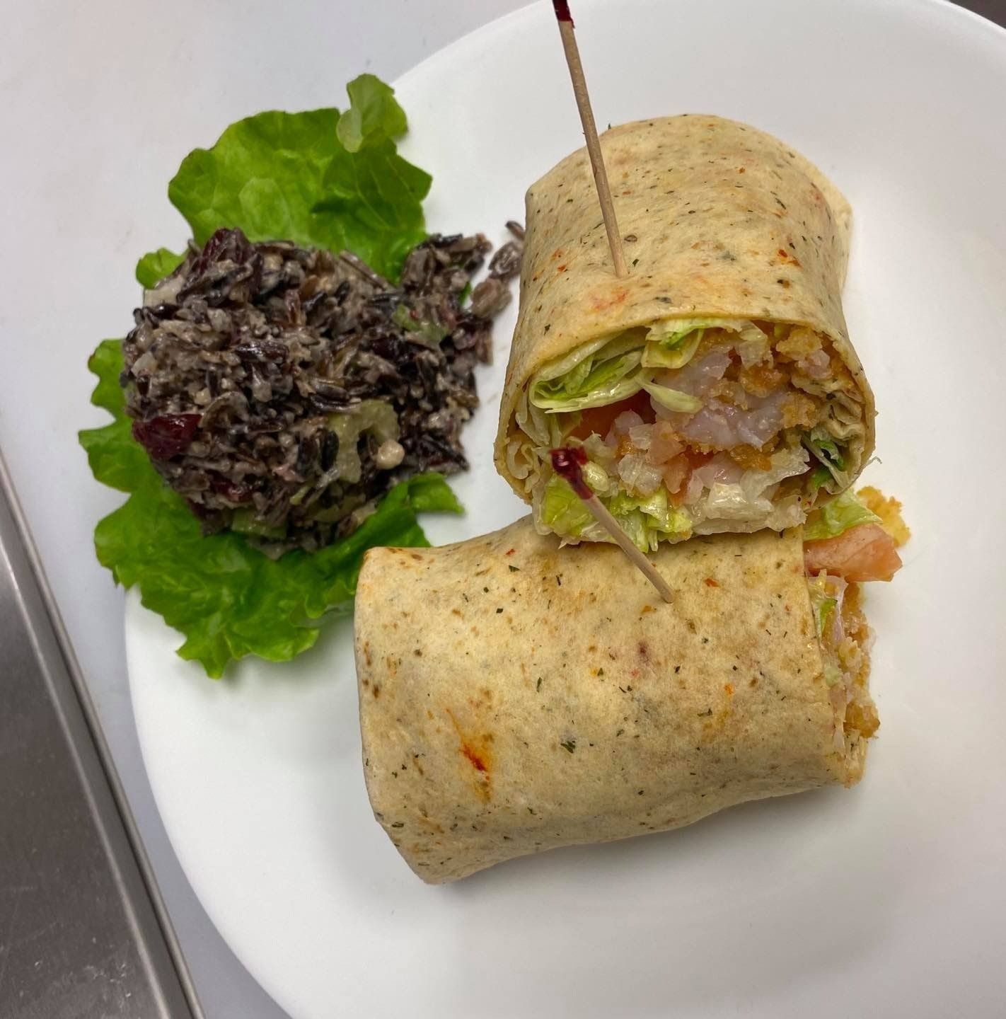 A tortilla wrap with lettuce and black rice on a white plate