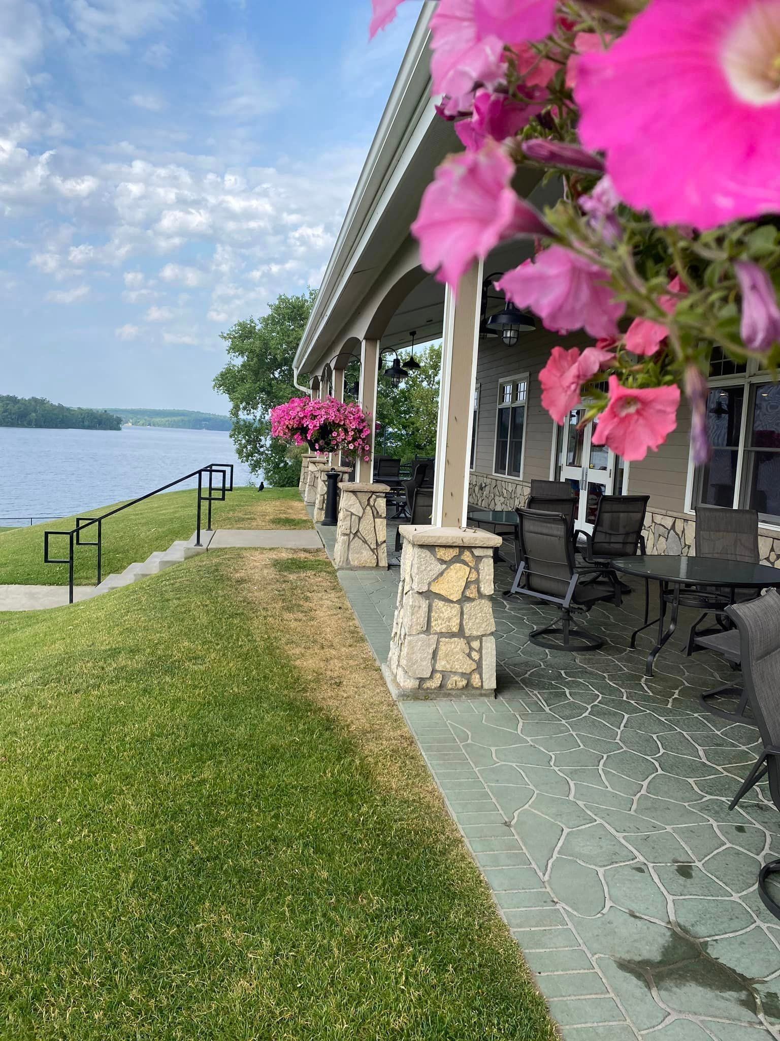 A house with a porch overlooking a lake with pink flowers in front of it.