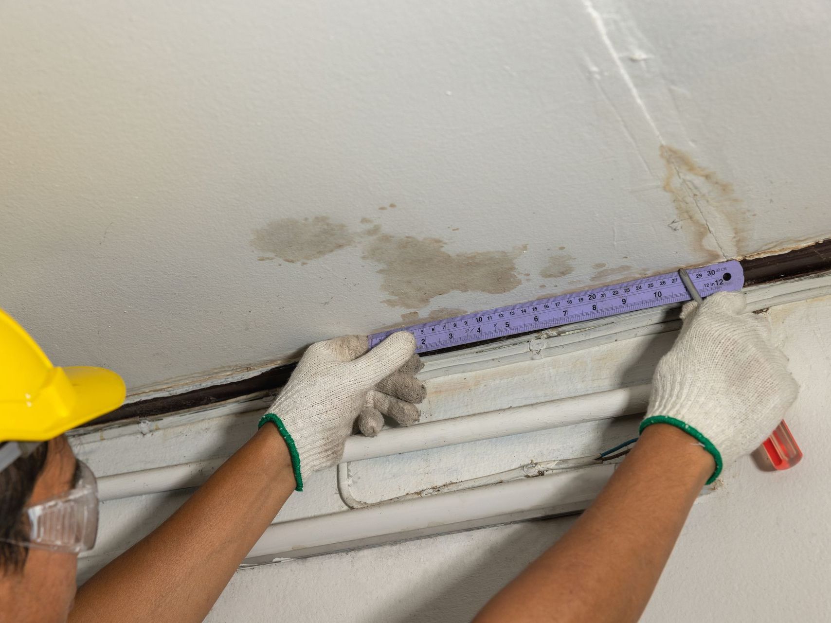 A man is measuring a ceiling with a ruler.