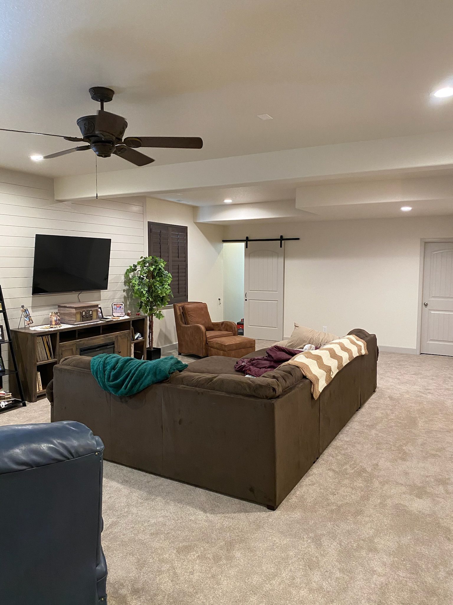 A living room with a couch , chair , television and ceiling fan.