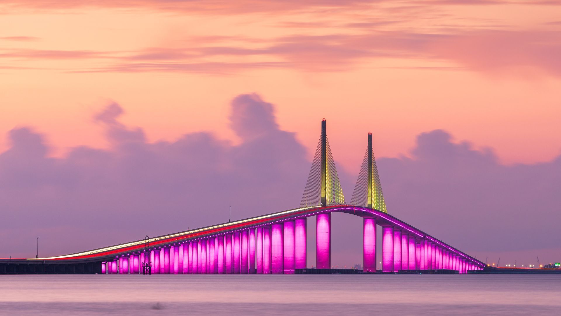 A bridge over a body of water at sunset with purple lights on it.