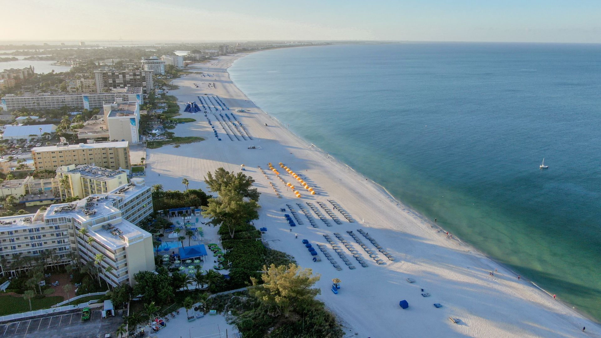 An aerial view of a beach with umbrellas and a city in the background.