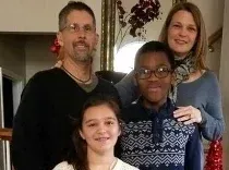 Family portrait indoors: man, woman, and two children smiling.