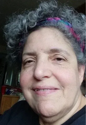 Woman with curly gray hair, wearing a colorful headband, smiling at the camera.