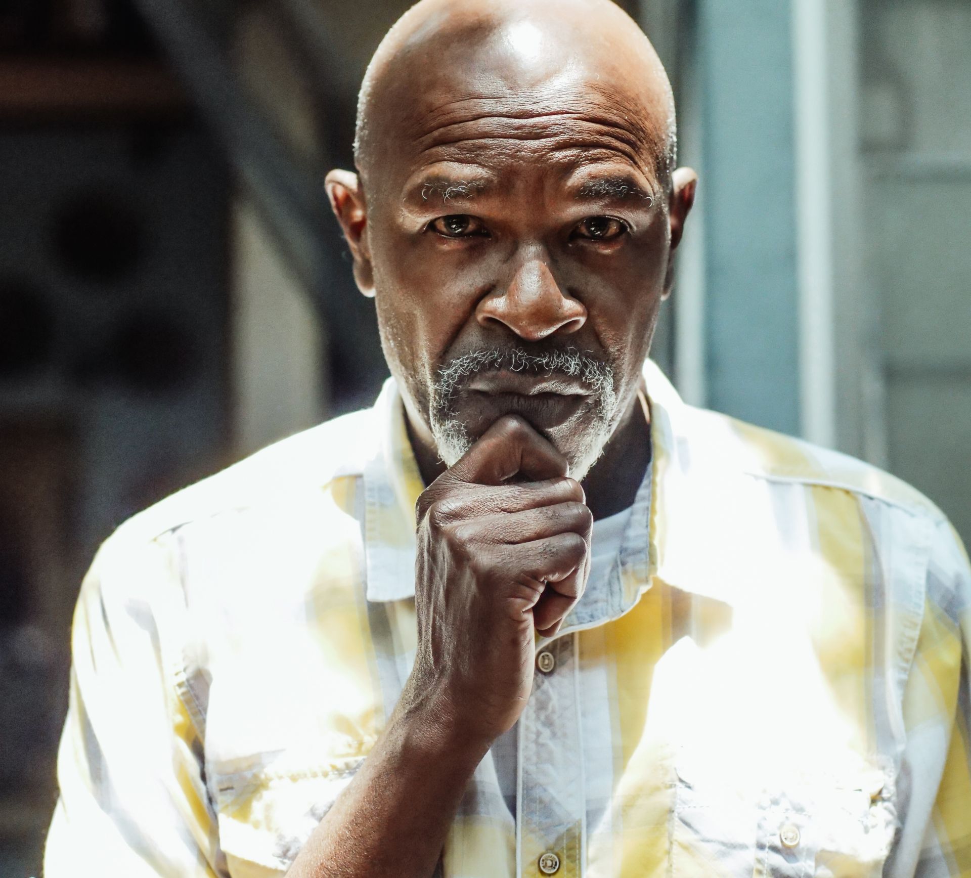 Bald Black man with a graying goatee, hand on chin, looking contemplative. Yellow and white striped shirt.