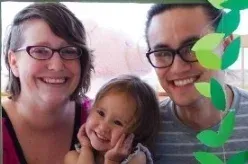 Family of three smiling, poses in a sunny environment. Leaves decorations frame the right side.
