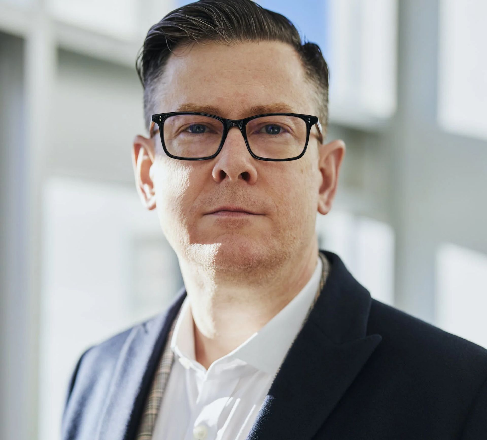 Man with glasses, dressed in a suit, looking directly at the camera.