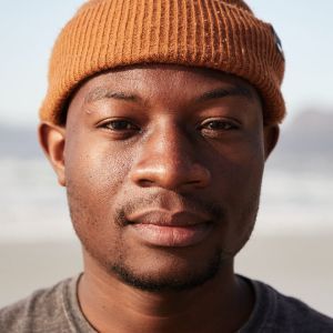 Man with brown beanie and grey shirt looking directly at the camera outdoors.