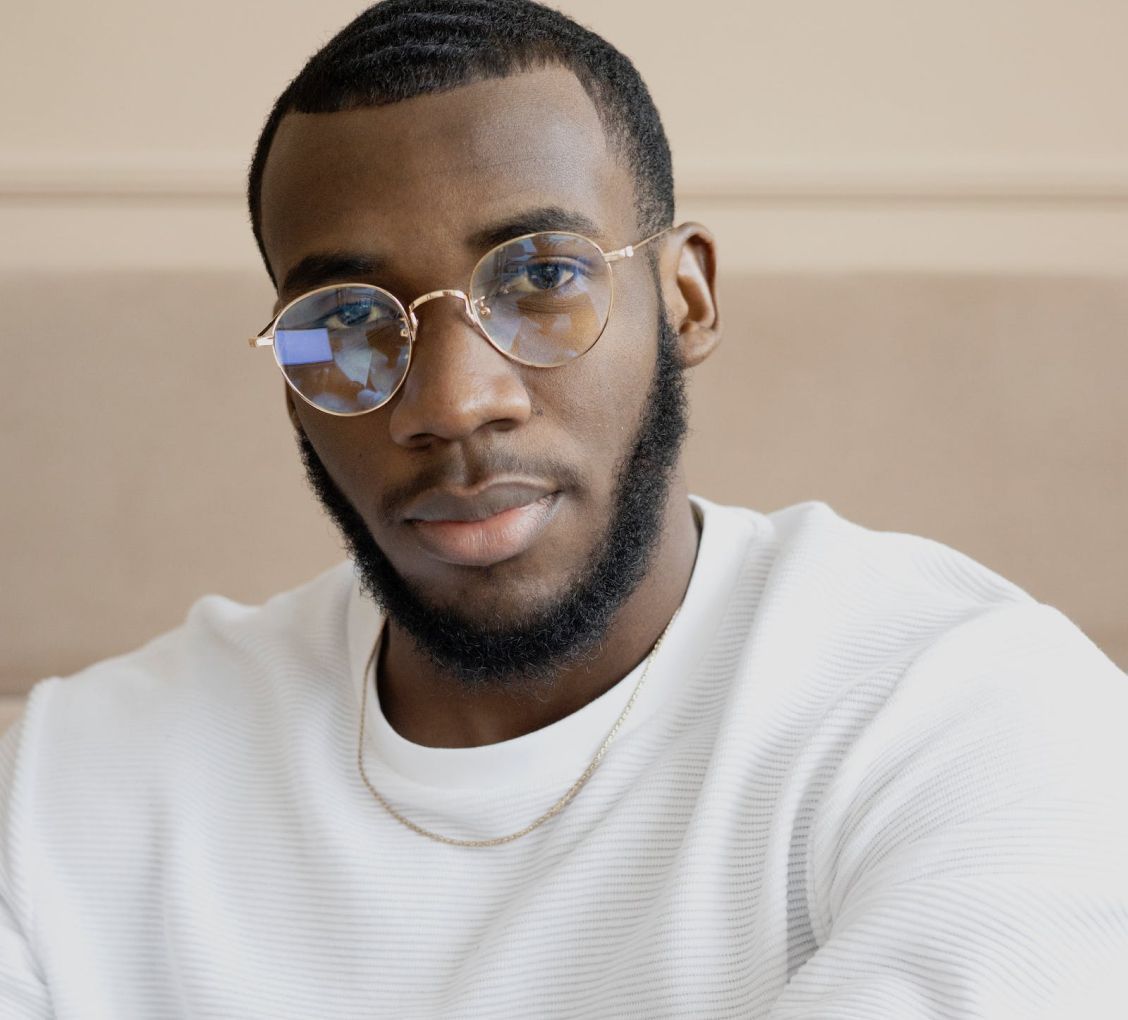 Man with glasses, looking at the camera, wearing a white sweater and gold chain.