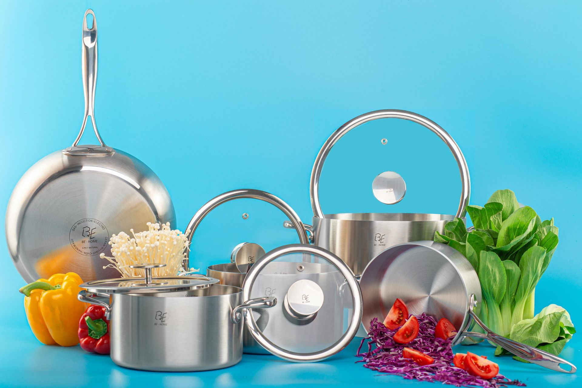 Stainless steel cookware set with vegetables on blue background.