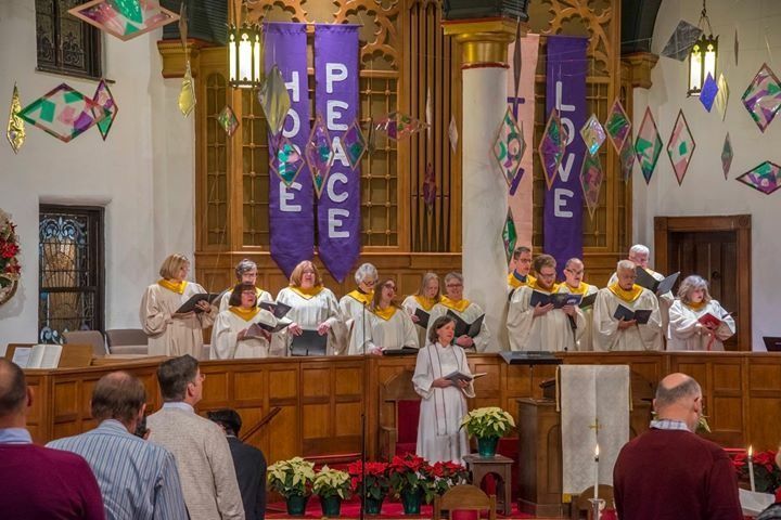 Choir in robes singing in a church. Purple banners read 