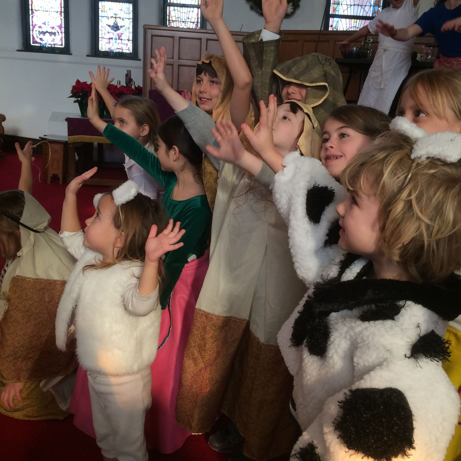 Children in costumes raise hands in a church during a play.