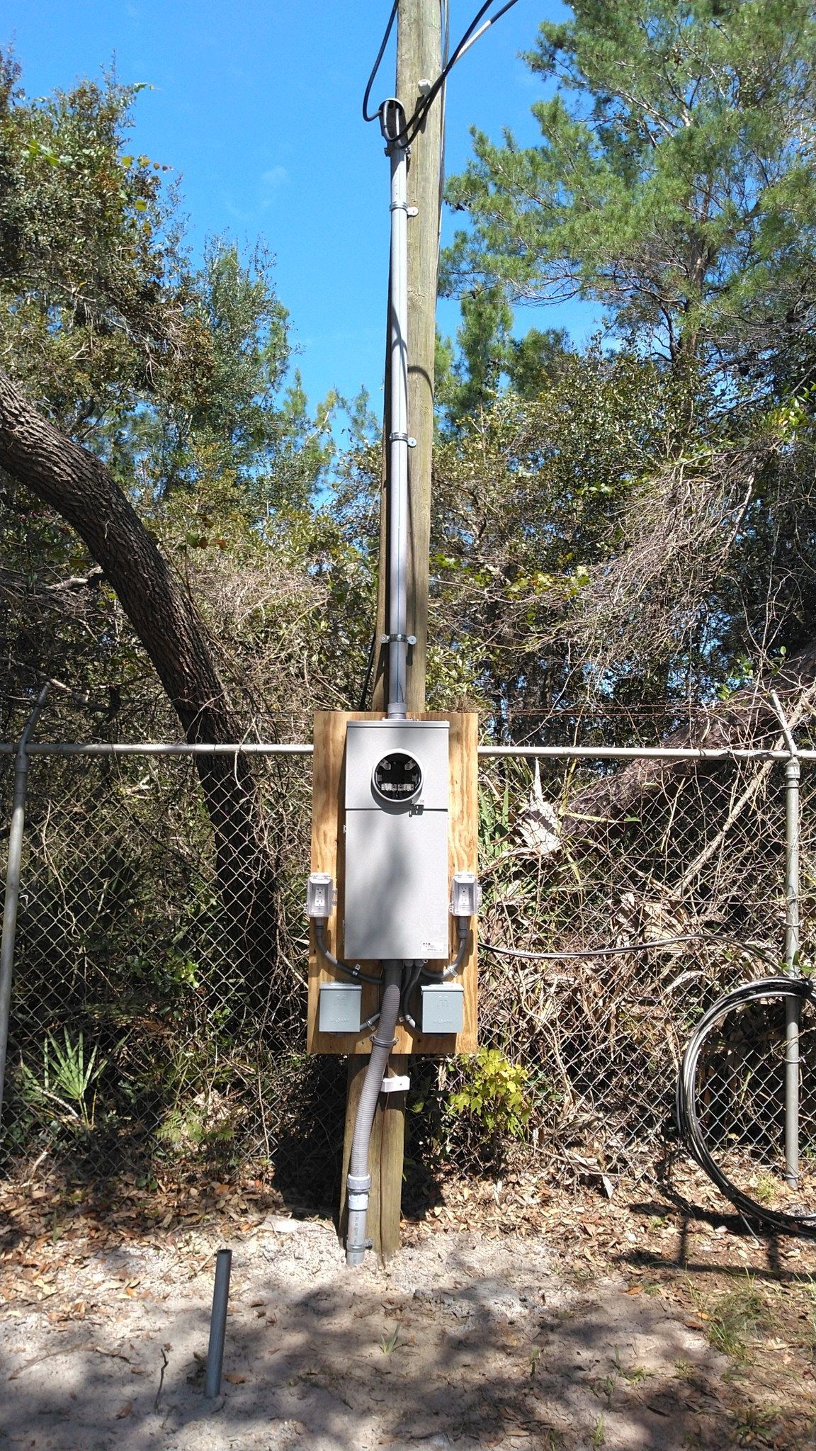 Utility pole with electrical equipment attached, including a metal box, mounted on a wooden structure.