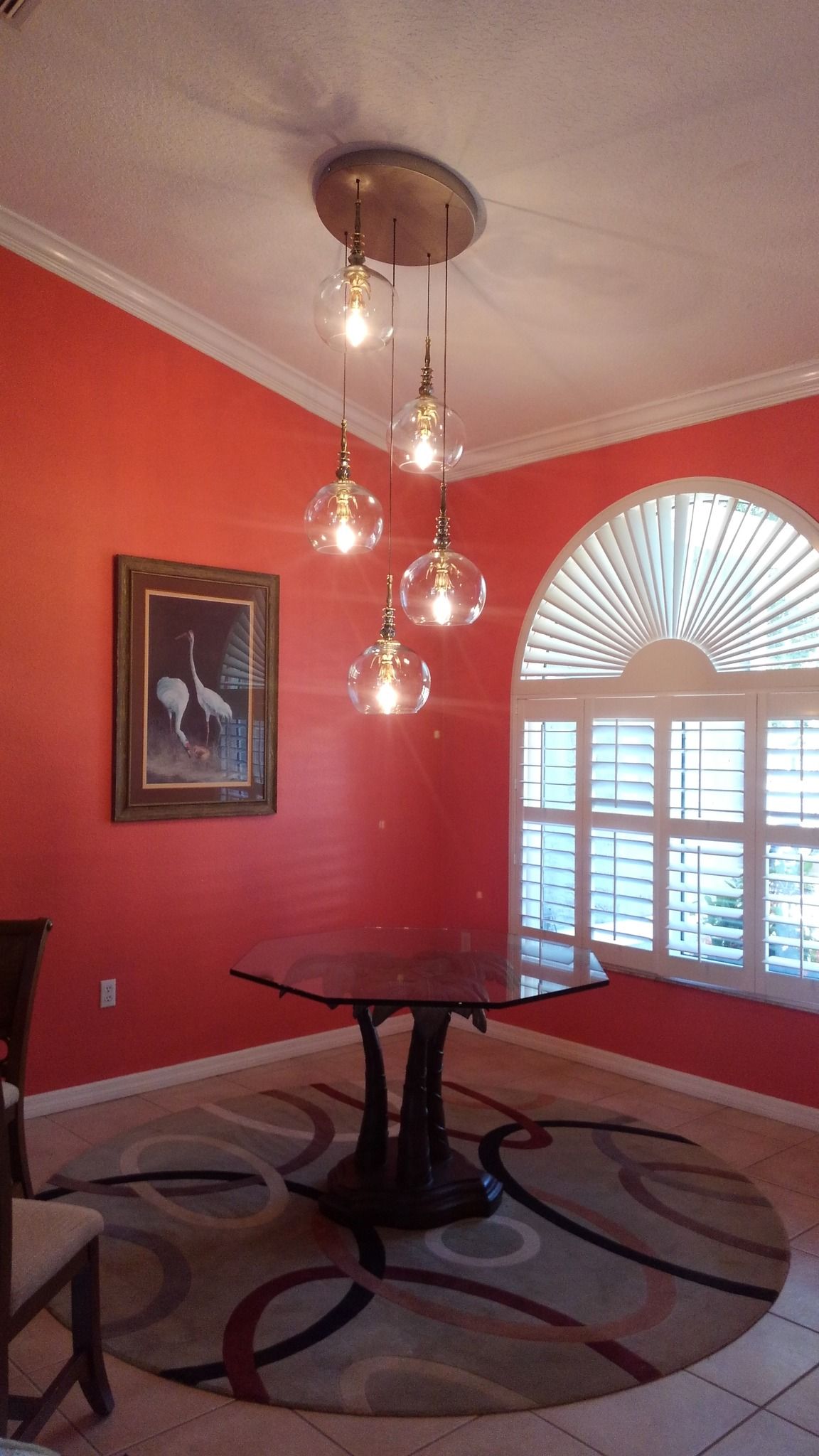 Dining room with red walls, round table, modern chandelier, and a patterned rug.