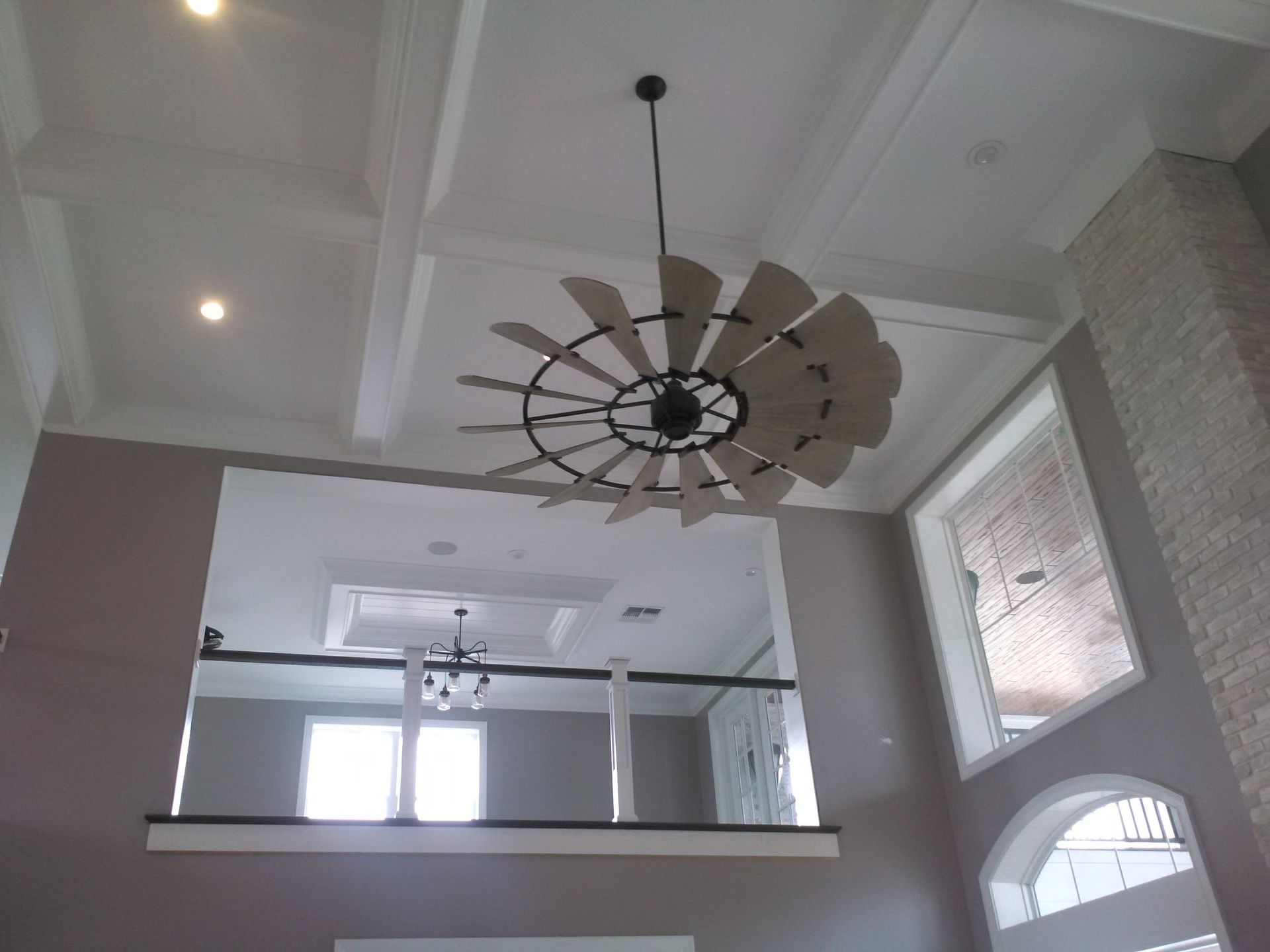 A modern home interior with high ceilings, a large windmill-style ceiling fan, and a second-floor overlook.