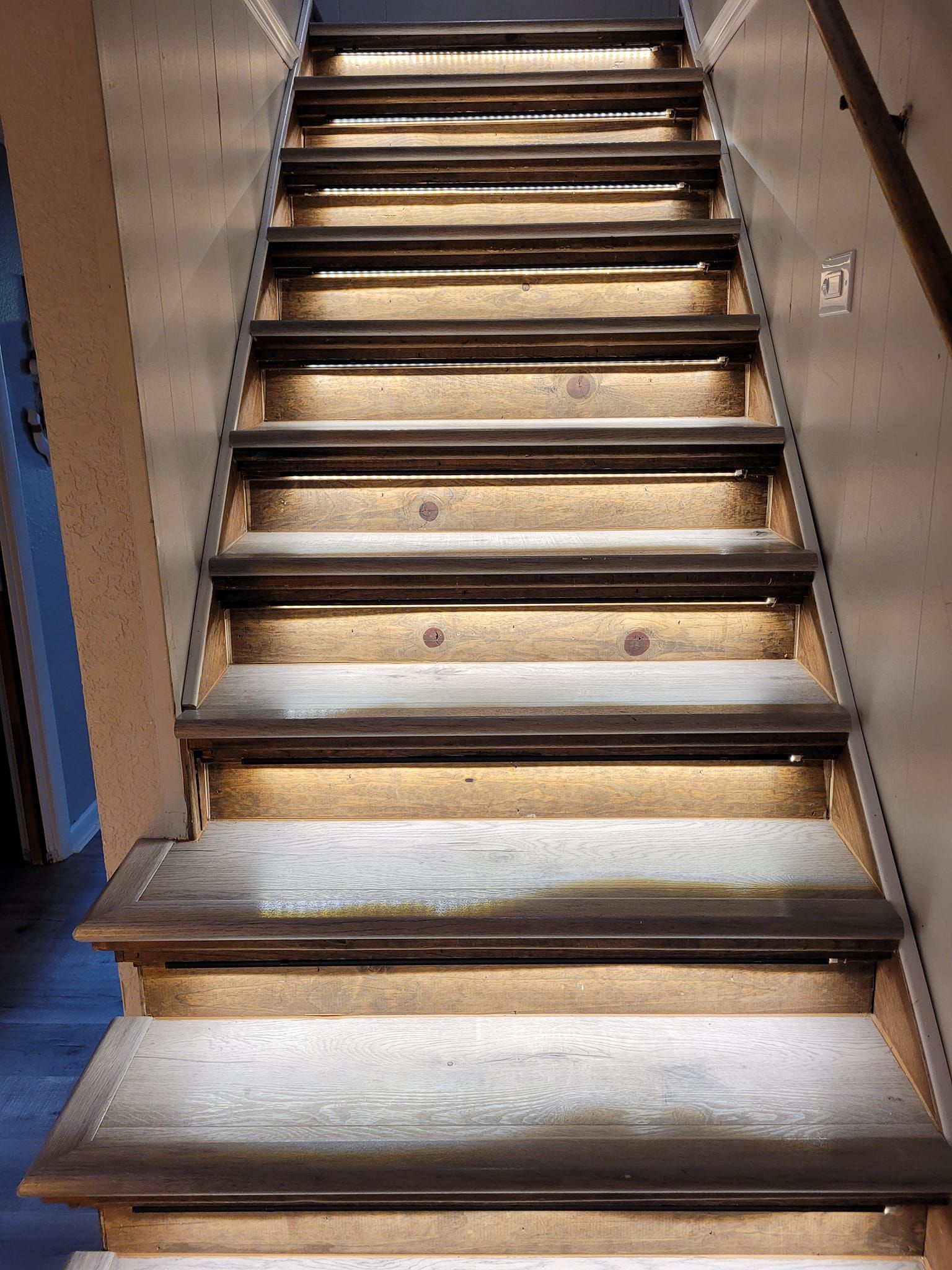 Staircase with built-in under-step lighting, dark wooden treads, and beige risers, ascending.