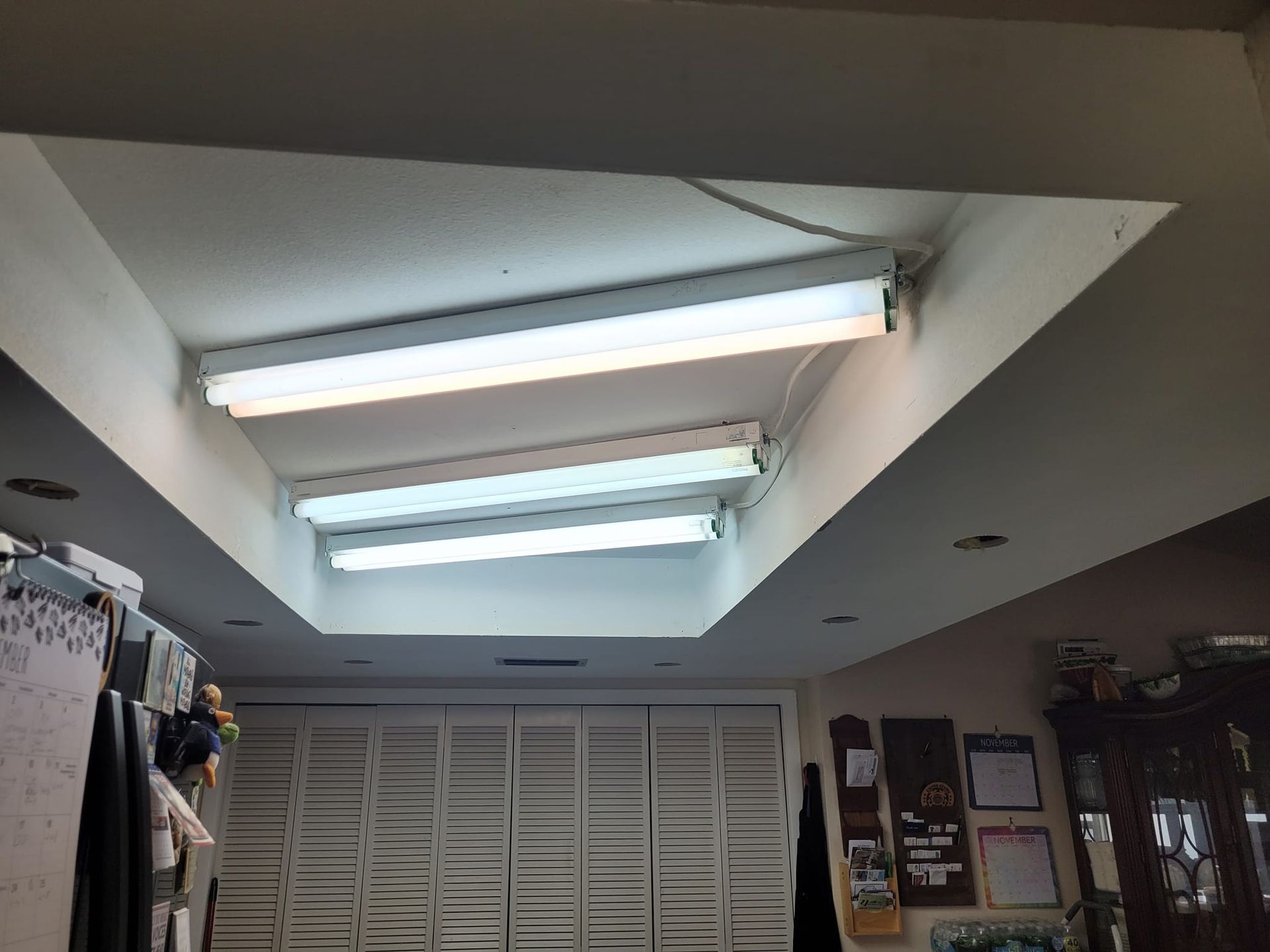 White ceiling with fluorescent lights in a recessed area above closed white shutters.