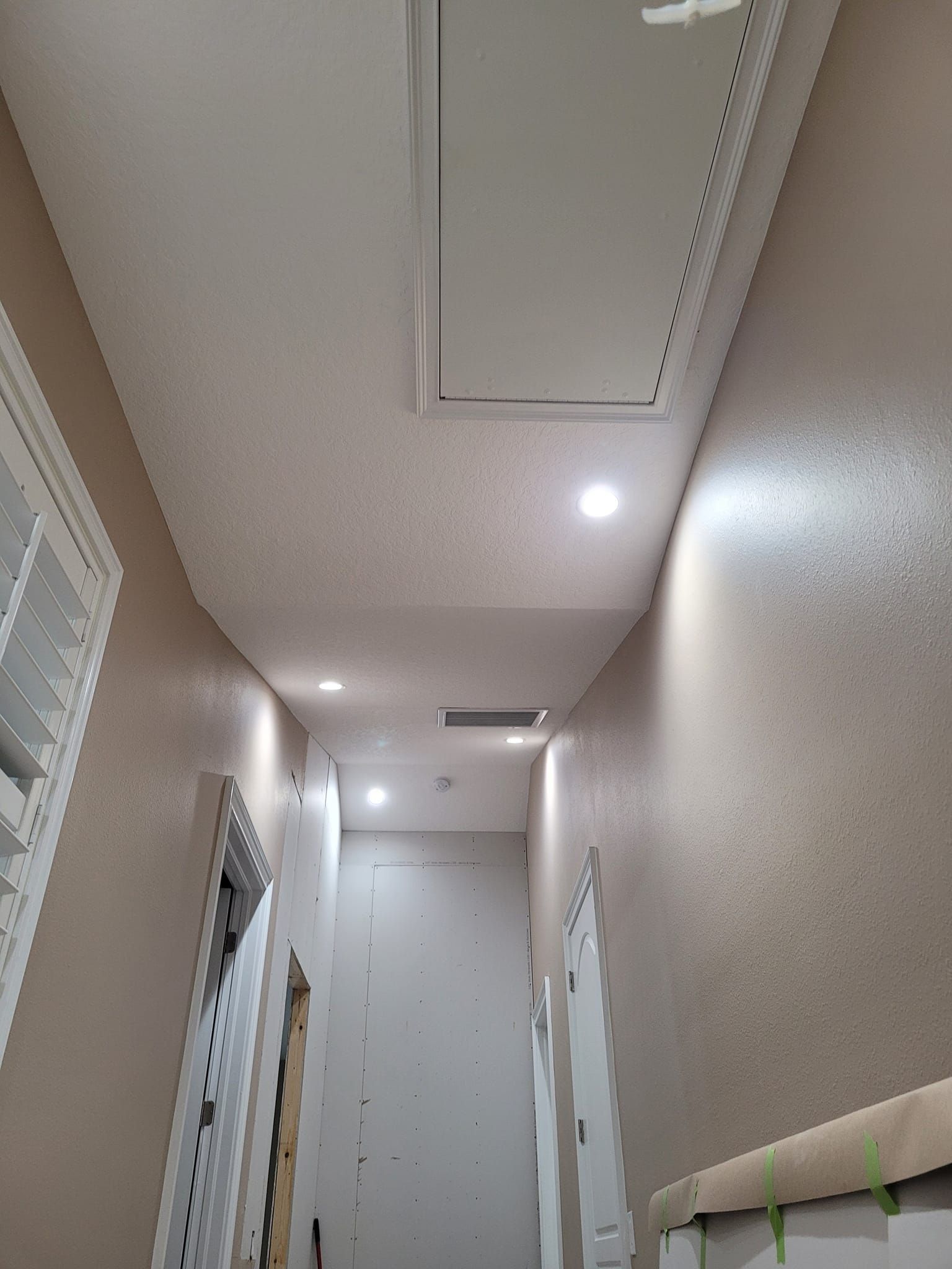 Narrow hallway with recessed lighting, an access hatch, and a partially-framed door.