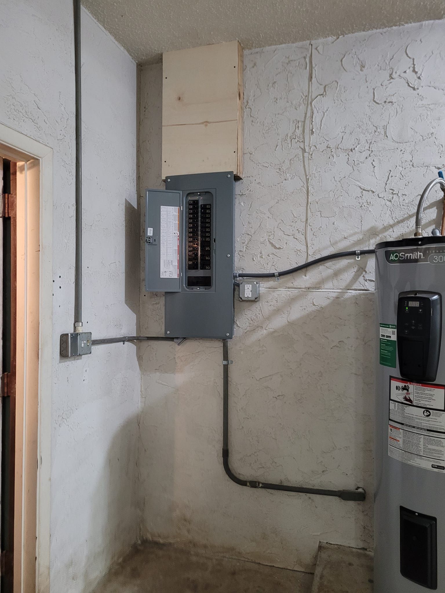 Electrical panel mounted on a light-colored wall in a basement with conduit running to a box.
