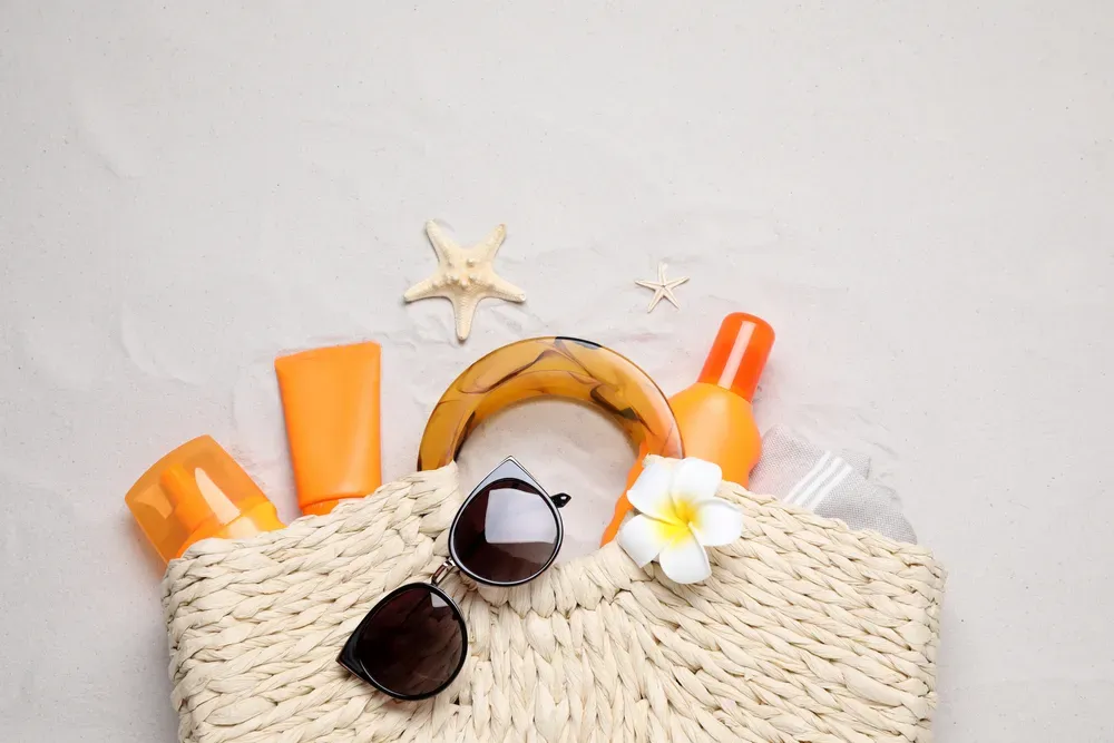 A wicker bag filled with sunscreen , sunglasses , and a flower.